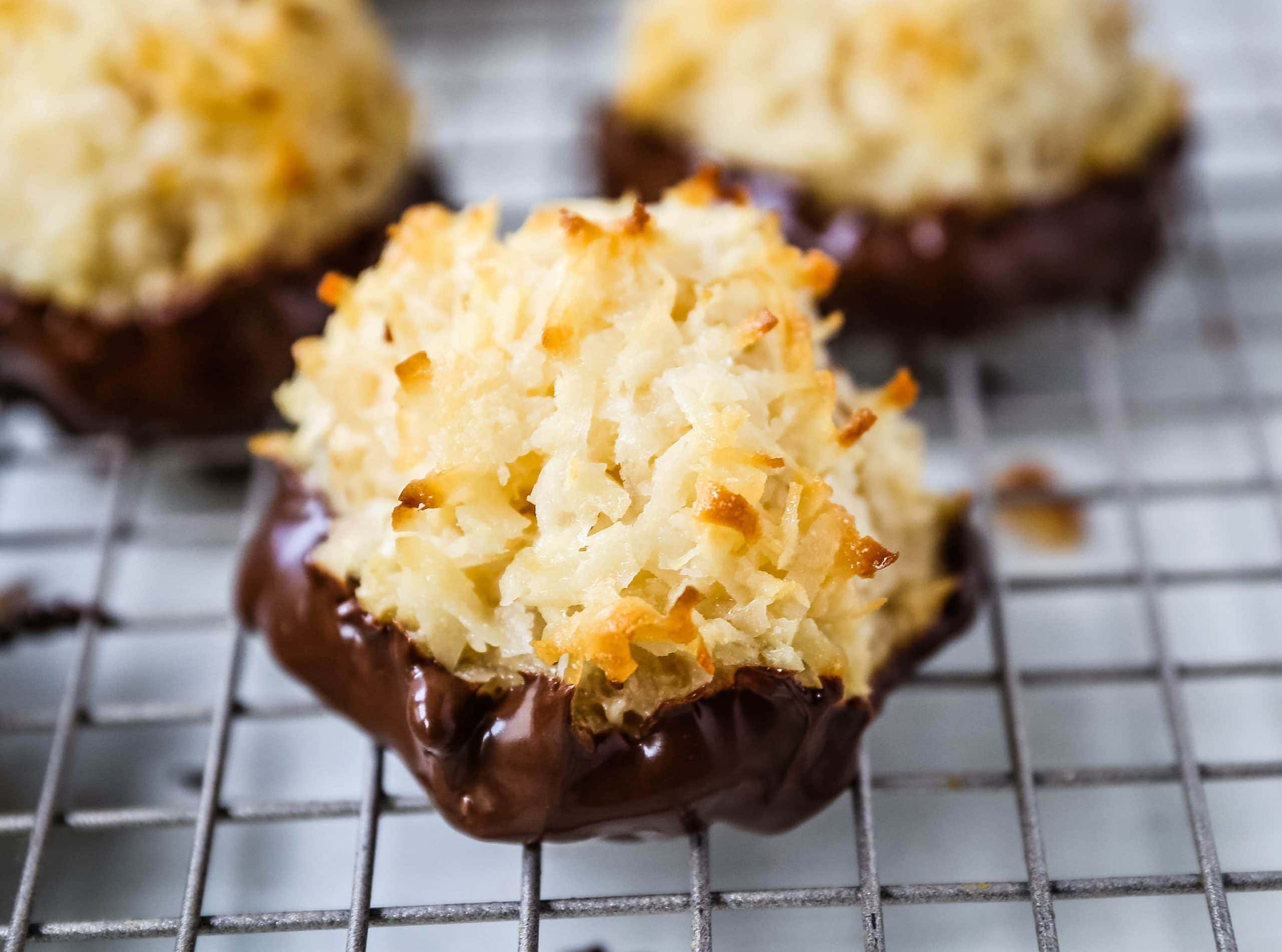 A tray of golden coconut macaroon biscuits on a parchment-lined baking sheet on a warm-toned kitchen counter, soft centers with crisp toasted edges