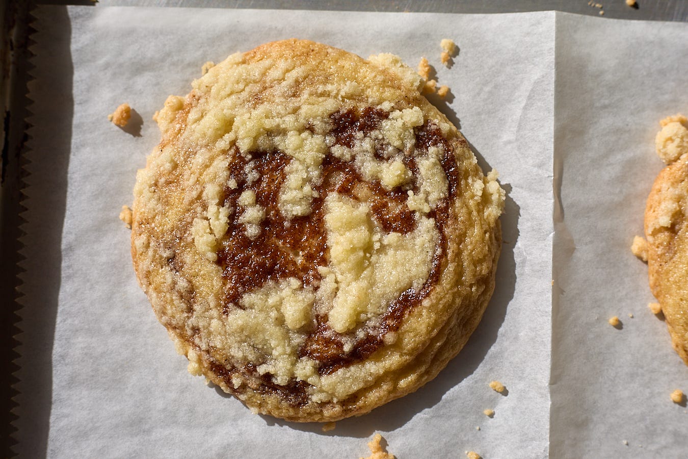 A tray of golden cookies with a crumbly streusel topping on a parchment-lined baking sheet on a warm kitchen counter