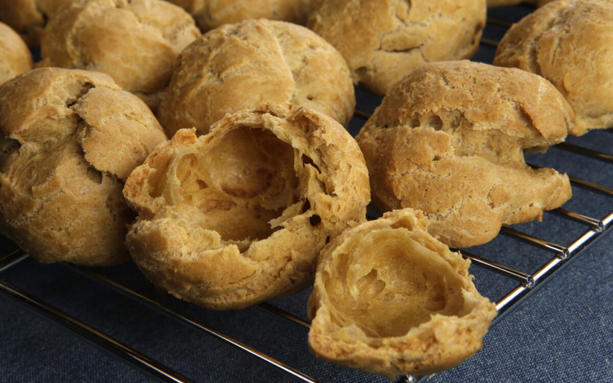 A tray of golden cream puff shells cooling on a parchment-lined baking sheet on a warm, softly lit kitchen counter