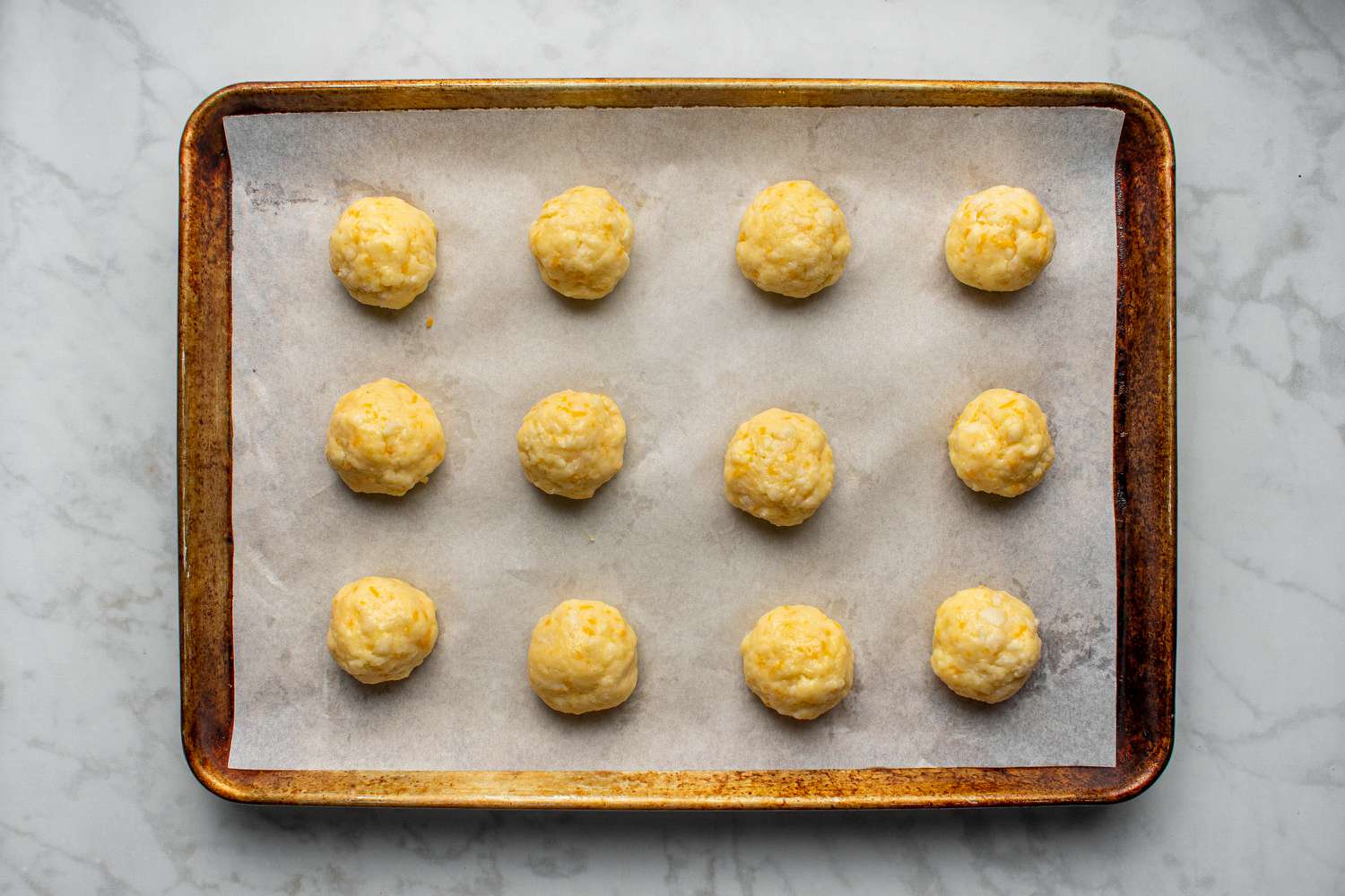 A tray of golden pão de queijo cheese breads fresh from the oven on a parchment-lined baking sheet on a warm kitchen counter