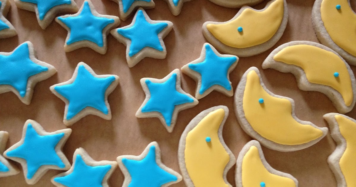 A tray of moon and star shaped sugar cookies decorated with white and navy icing on a warm kitchen counter, cozy evening lighting