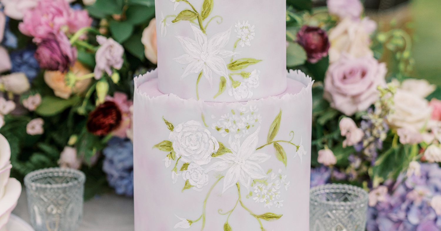 A two-tier frosted wedding cake on a cake stand with plates and forks set nearby for serving