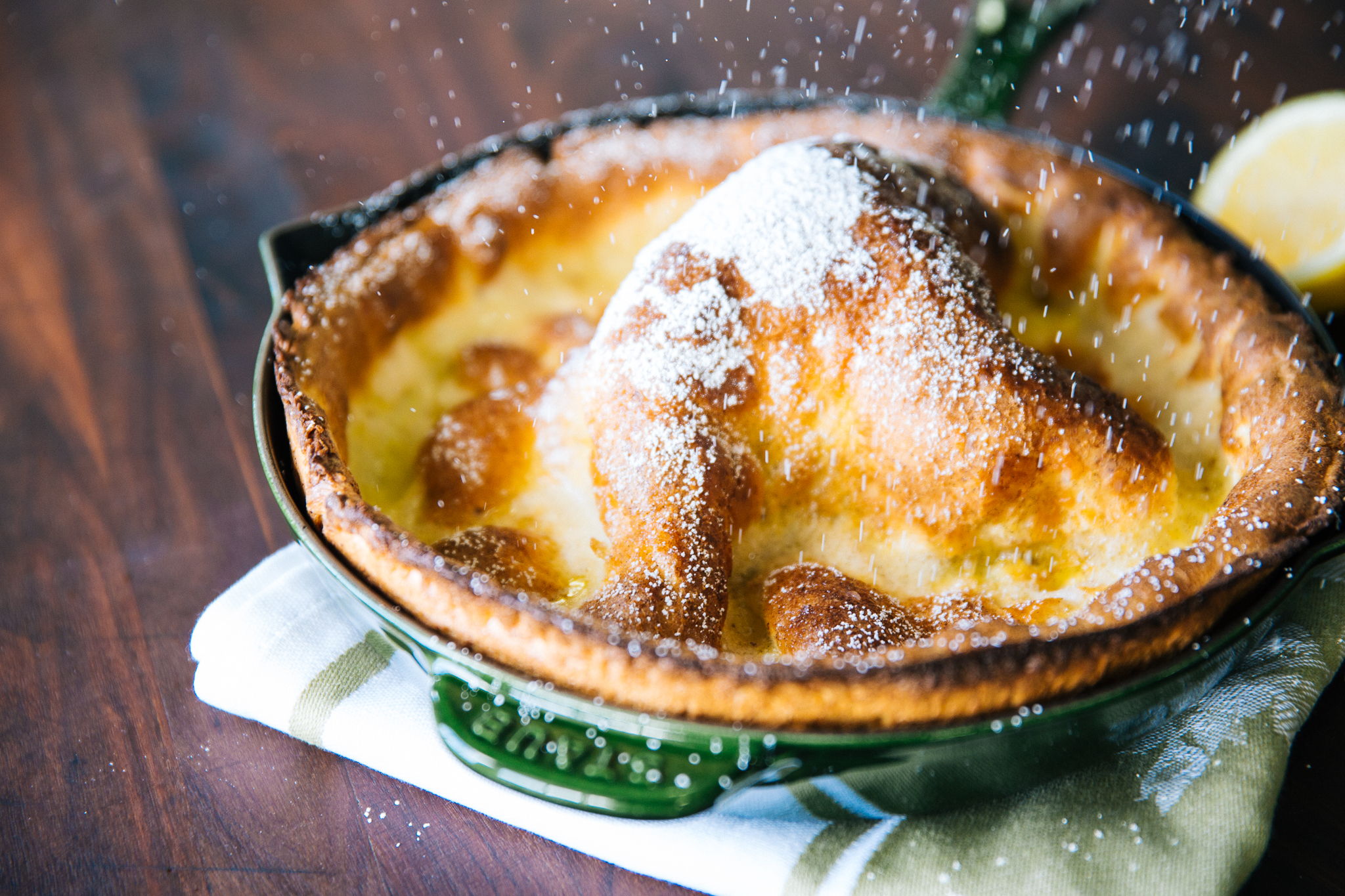A warm German pancake on a plate with lemon wedges and a light dusting of powdered sugar on a wooden breakfast table