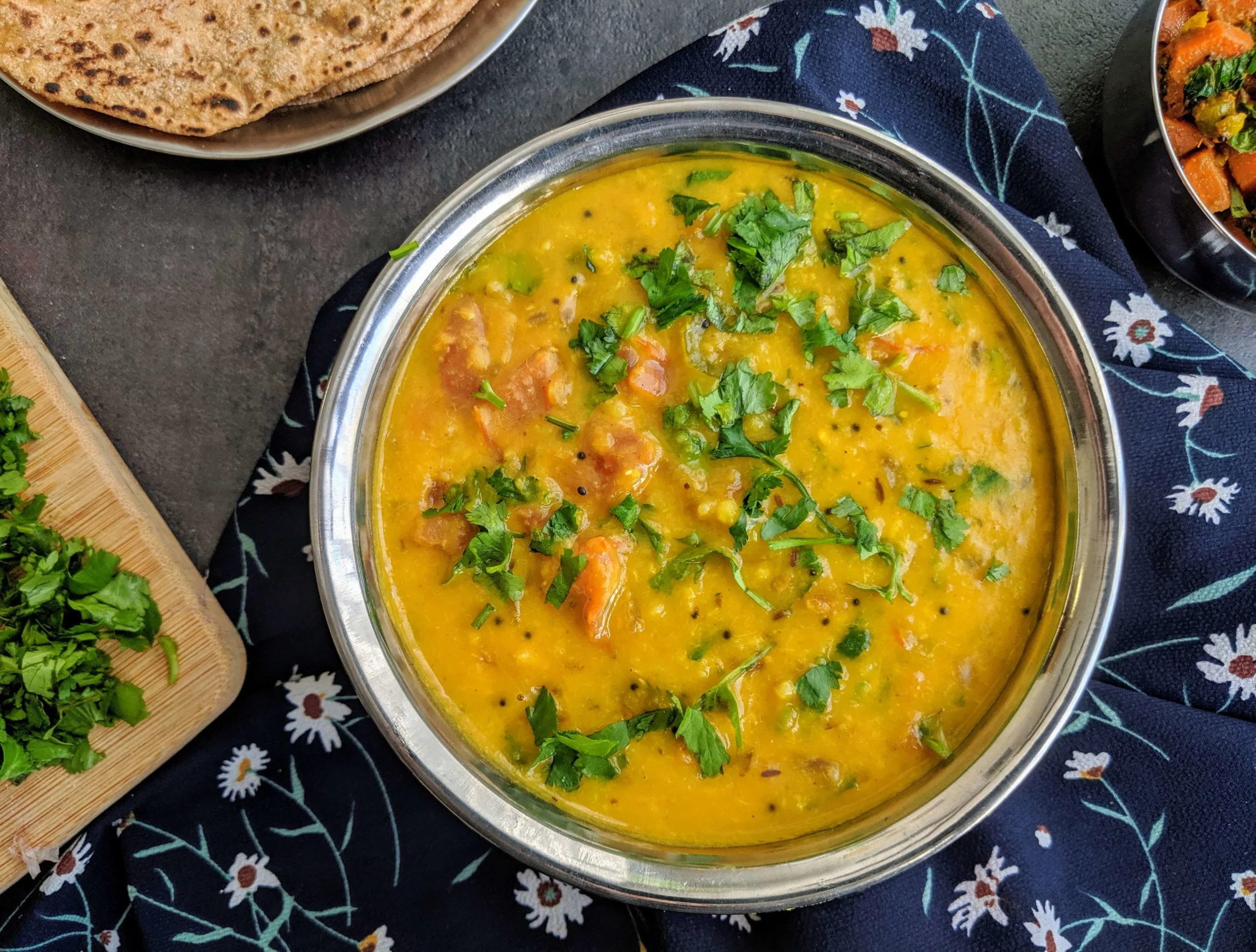 A warm bowl of creamy yellow moong dal tadka with a glossy cumin-garlic chili temper on top, served with rice on a simple wooden table in soft natural light