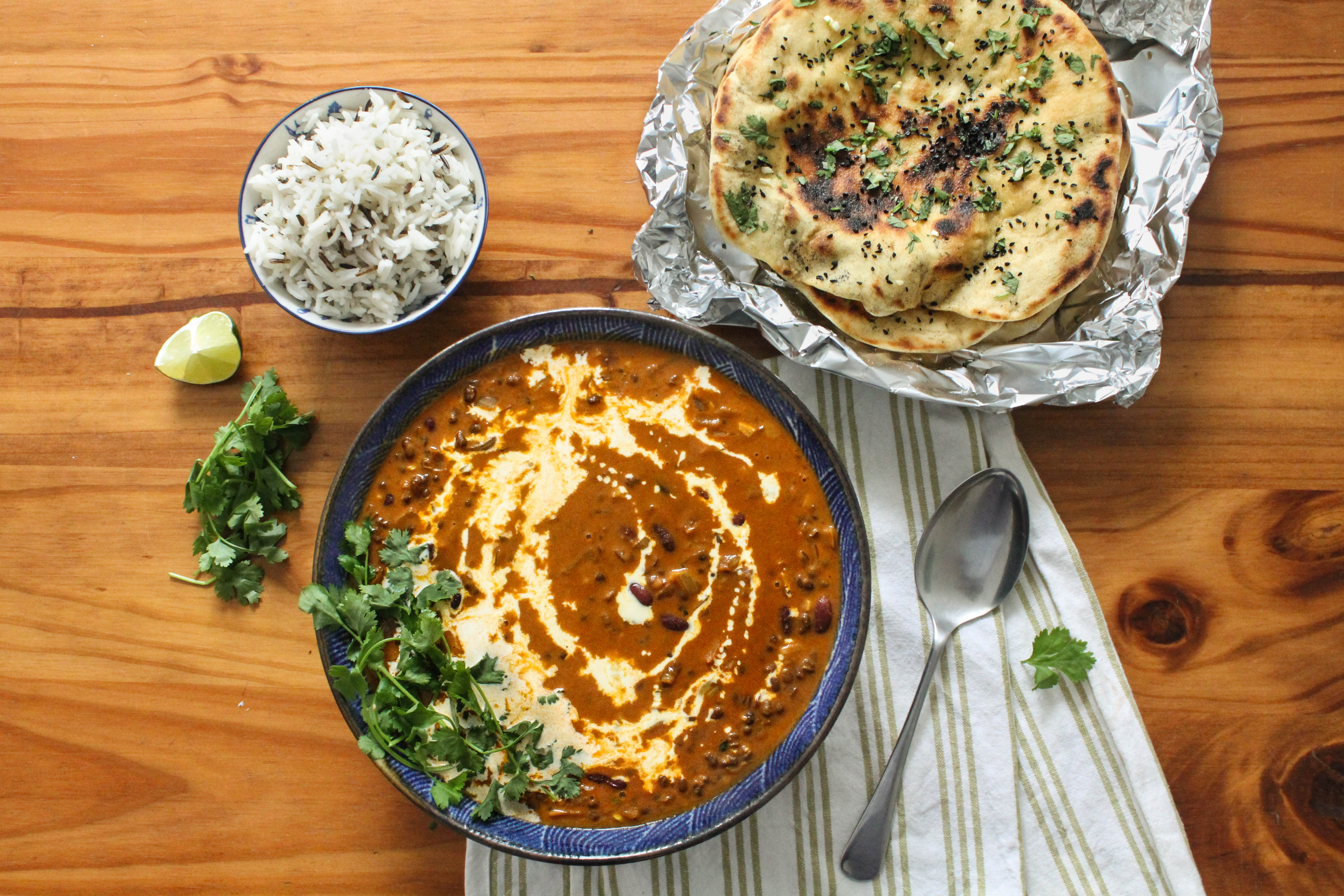 A warm bowl of dal makhni garnished with a swirl of cream, a pat of butter, and chopped cilantro, served with naan on a wooden table in soft natural light