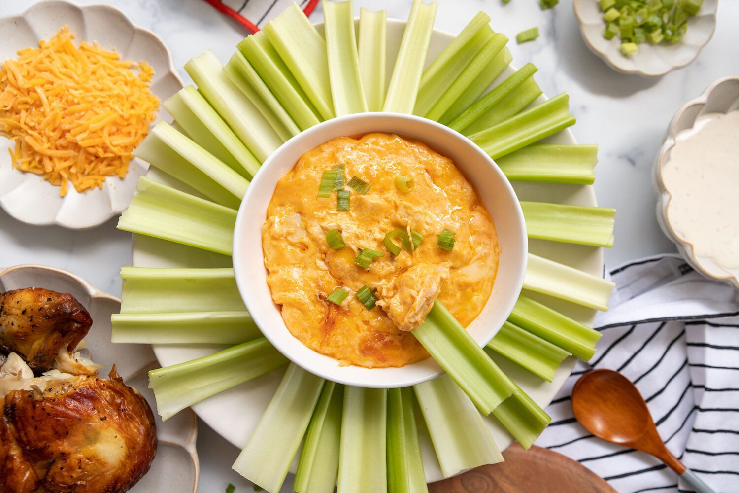 A warm dish of chicken wing dip on a table with celery sticks, carrot sticks, and tortilla chips ready for dipping