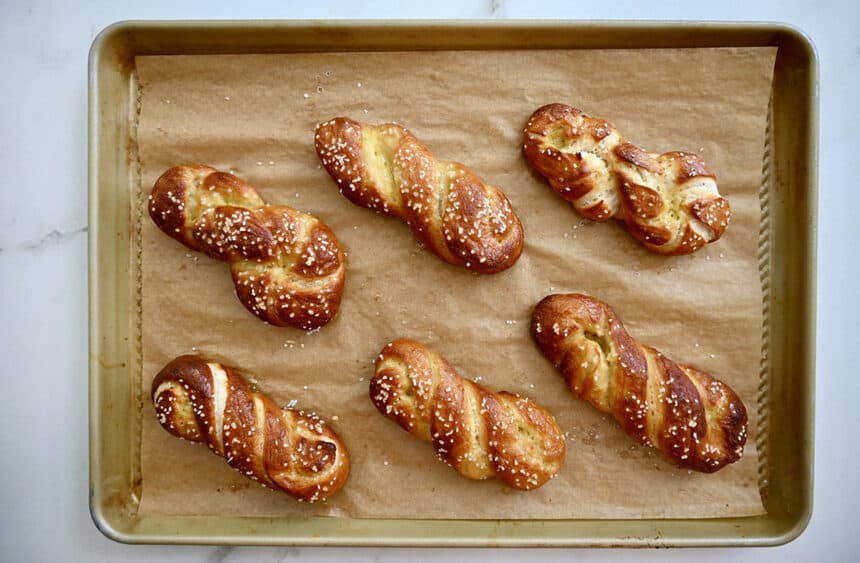 A warm, golden brown soft pretzel twist on parchment paper, brushed with melted butter and sprinkled with coarse salt on a cozy kitchen counter