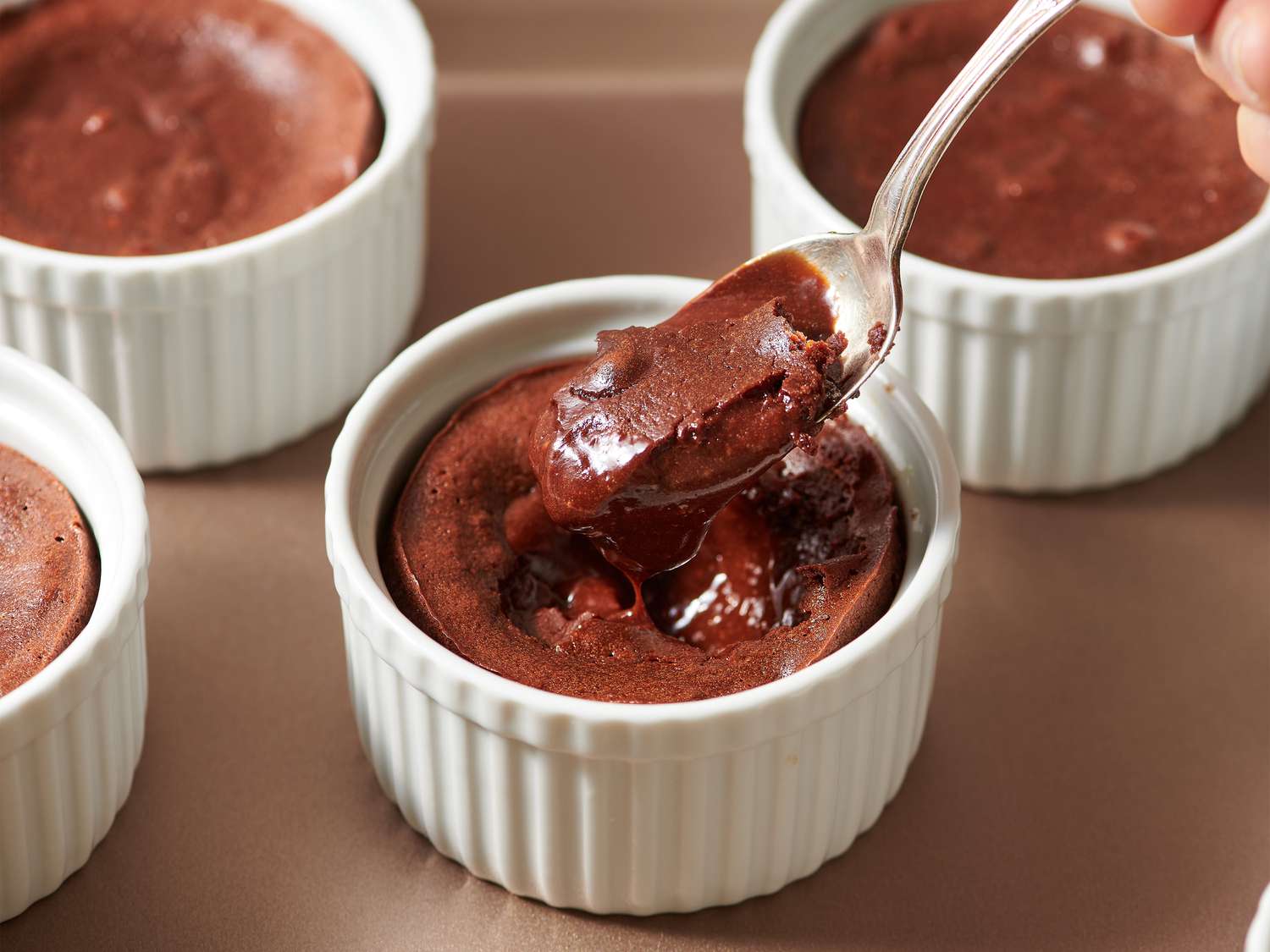 A warm molten chocolate lava cake on a white plate with a spoon cutting into the center as melted chocolate flows out, soft kitchen lighting