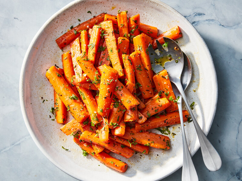 A warm serving bowl of glossy brown sugar glazed carrots sprinkled with chopped parsley on a wooden table under cozy kitchen lighting