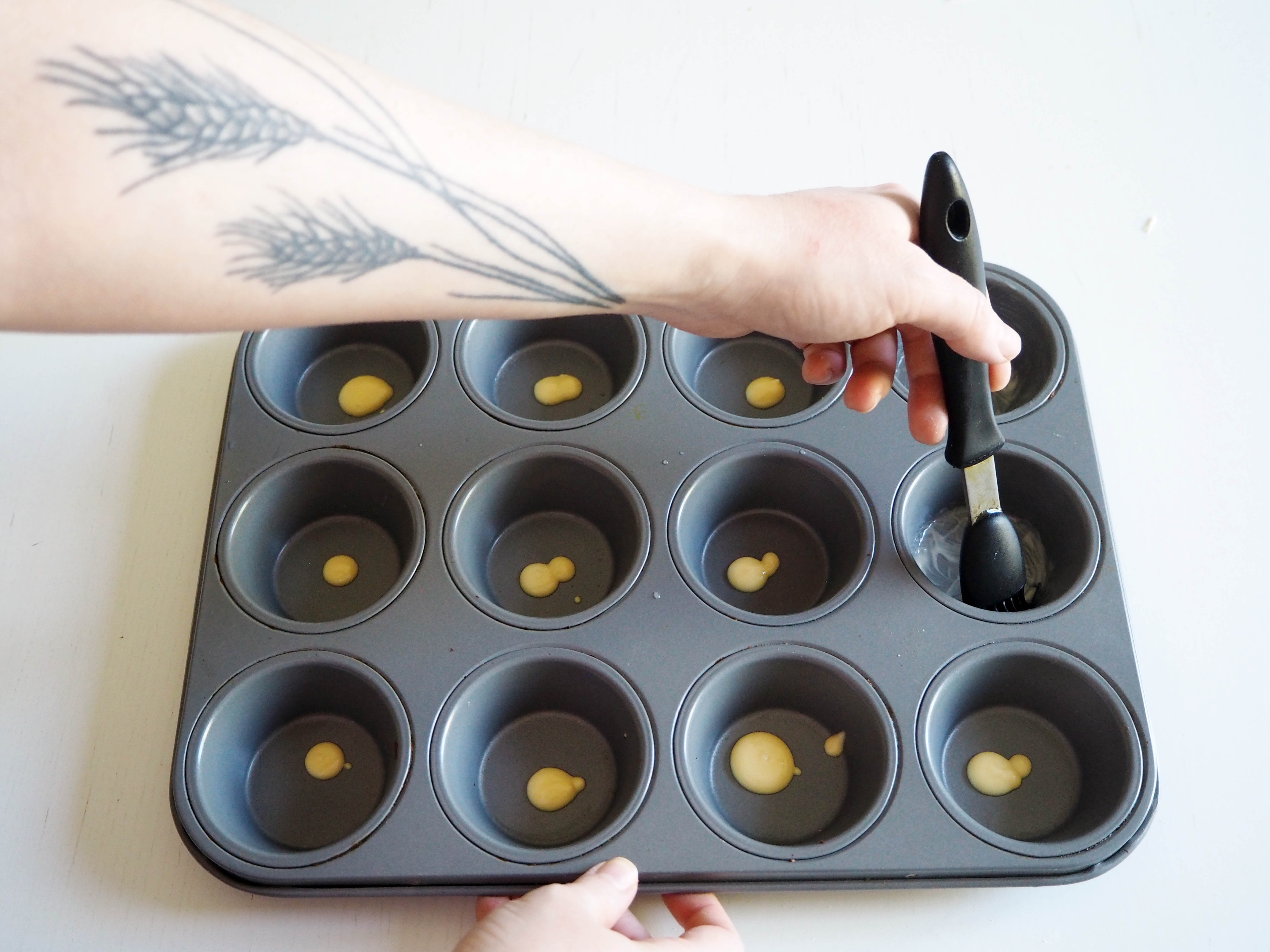 A well-greased metal muffin pan set beside a bowl of corn muffin batter, ready to be portioned