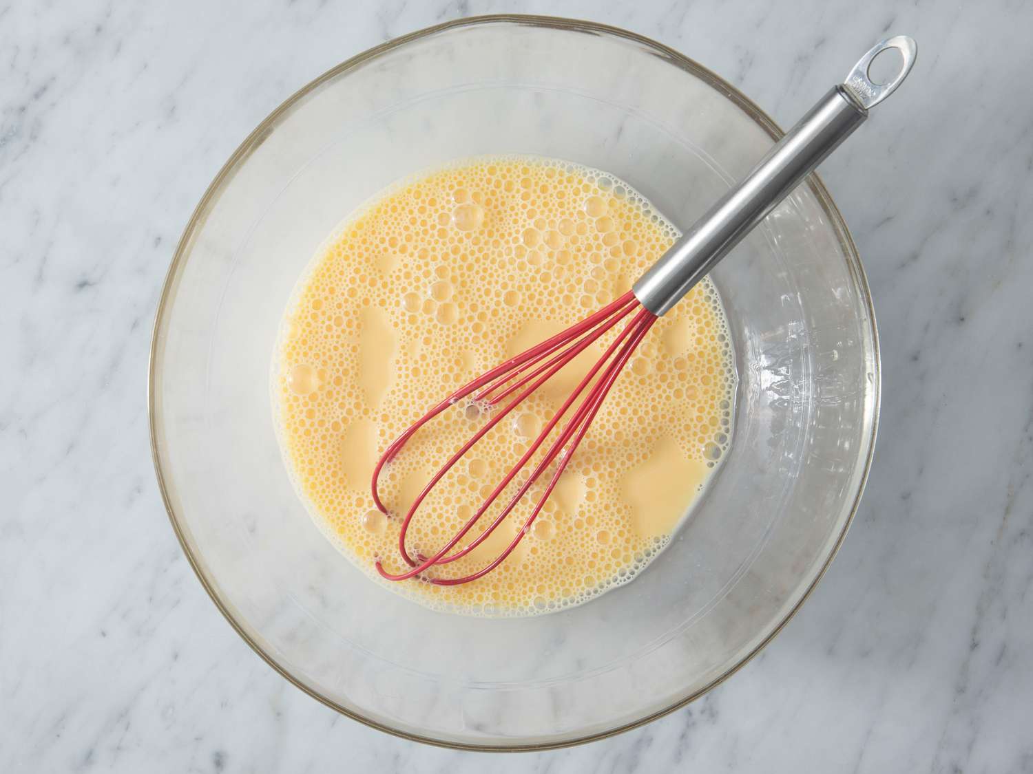 A whisk resting in a large mixing bowl on a tidy kitchen counter with measuring cups nearby