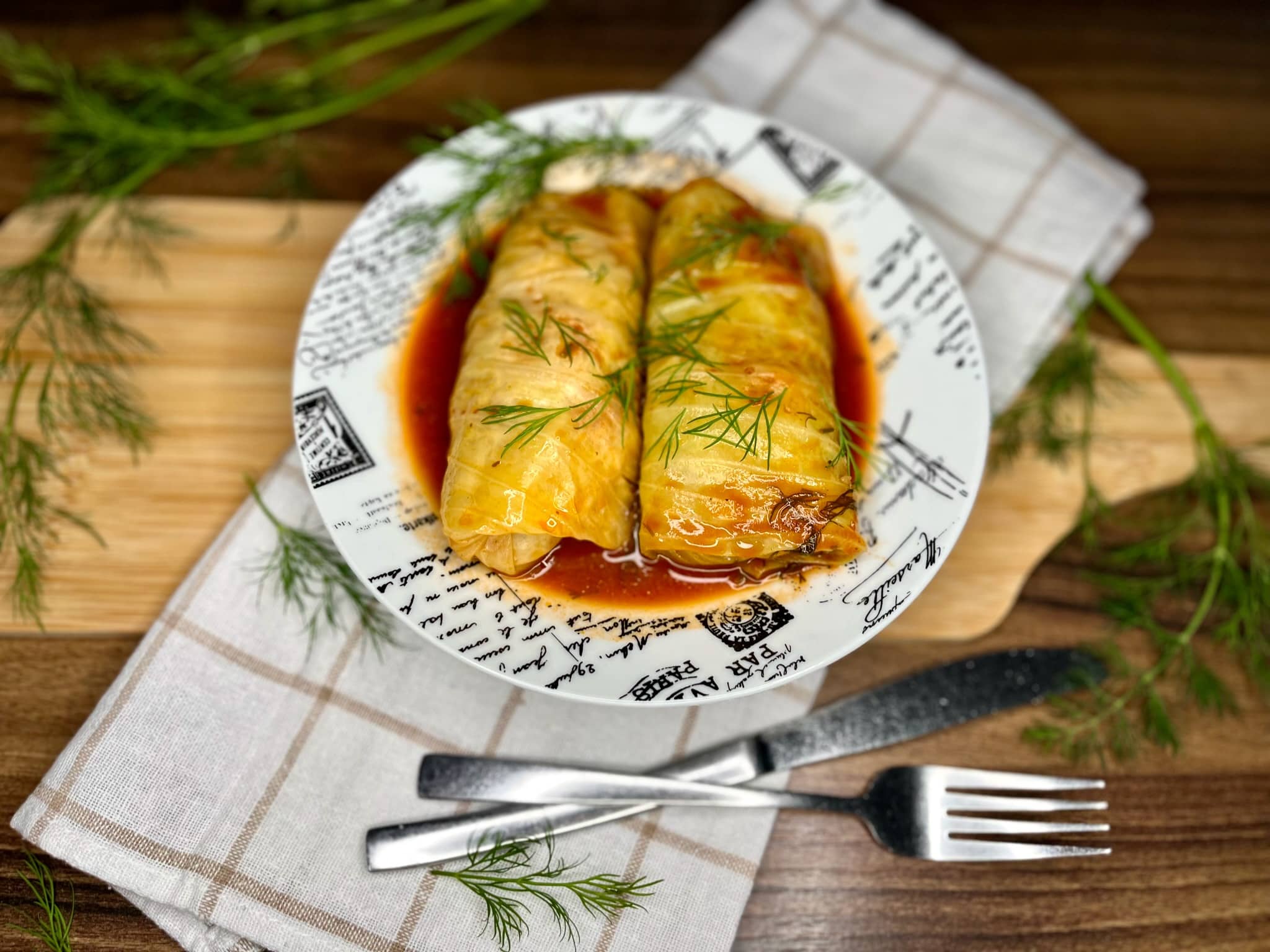 A white baking dish filled with golabki (Polish cabbage rolls) nestled in tomato sauce, steam rising, with a spoon scooping sauce at the edge