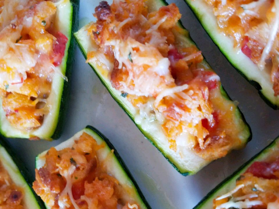 A white oval baking dish filled with zucchini boats stuffed with a tomatoey meat filling and topped with melted mozzarella, lightly browned on top on a warm kitchen counter
