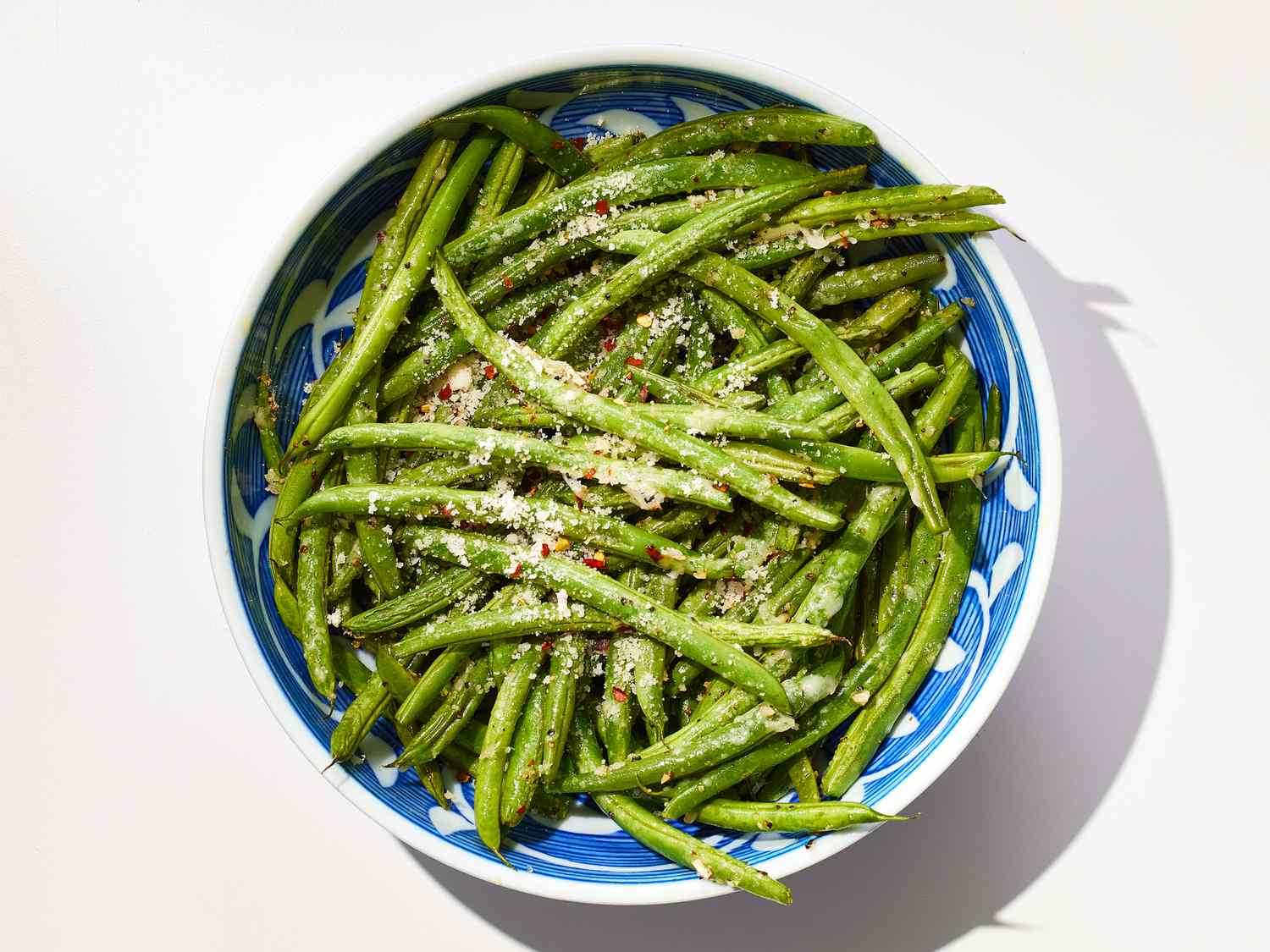 A white serving platter piled with baked green beans with toasted edges, grated Parmesan, and lemon wedges on a warm, softly lit kitchen table