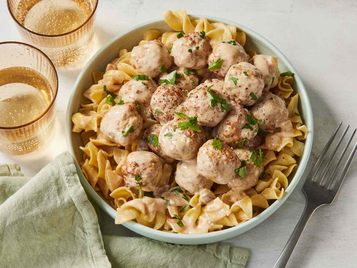 A white slow cooker filled with glossy saucy meatballs, a serving spoon resting on the edge, on a warm kitchen counter with soft natural light