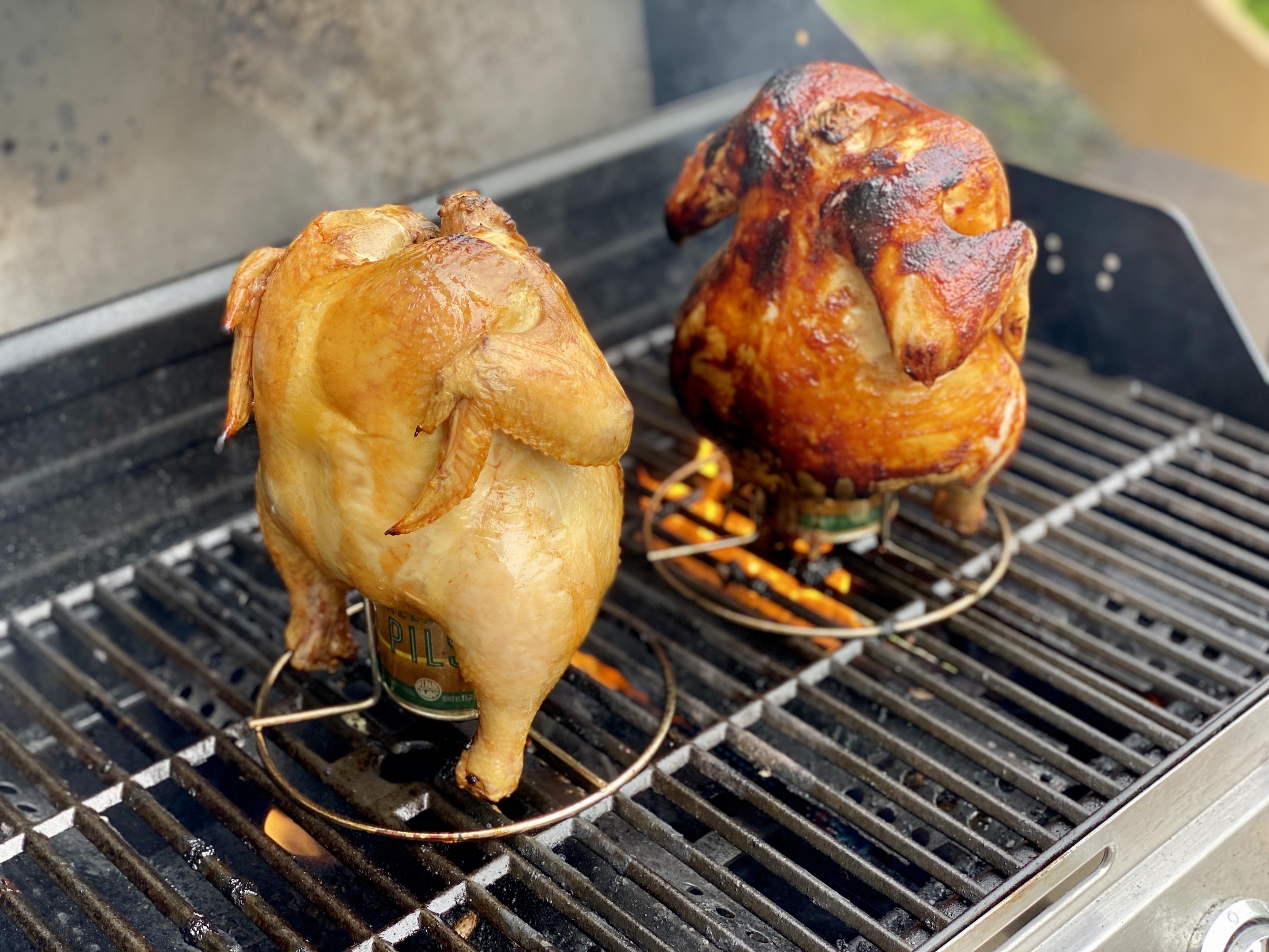 A whole beer can chicken with deeply browned, crispy skin resting on a cutting board with lemon wedges and fresh herbs on a warm kitchen counter