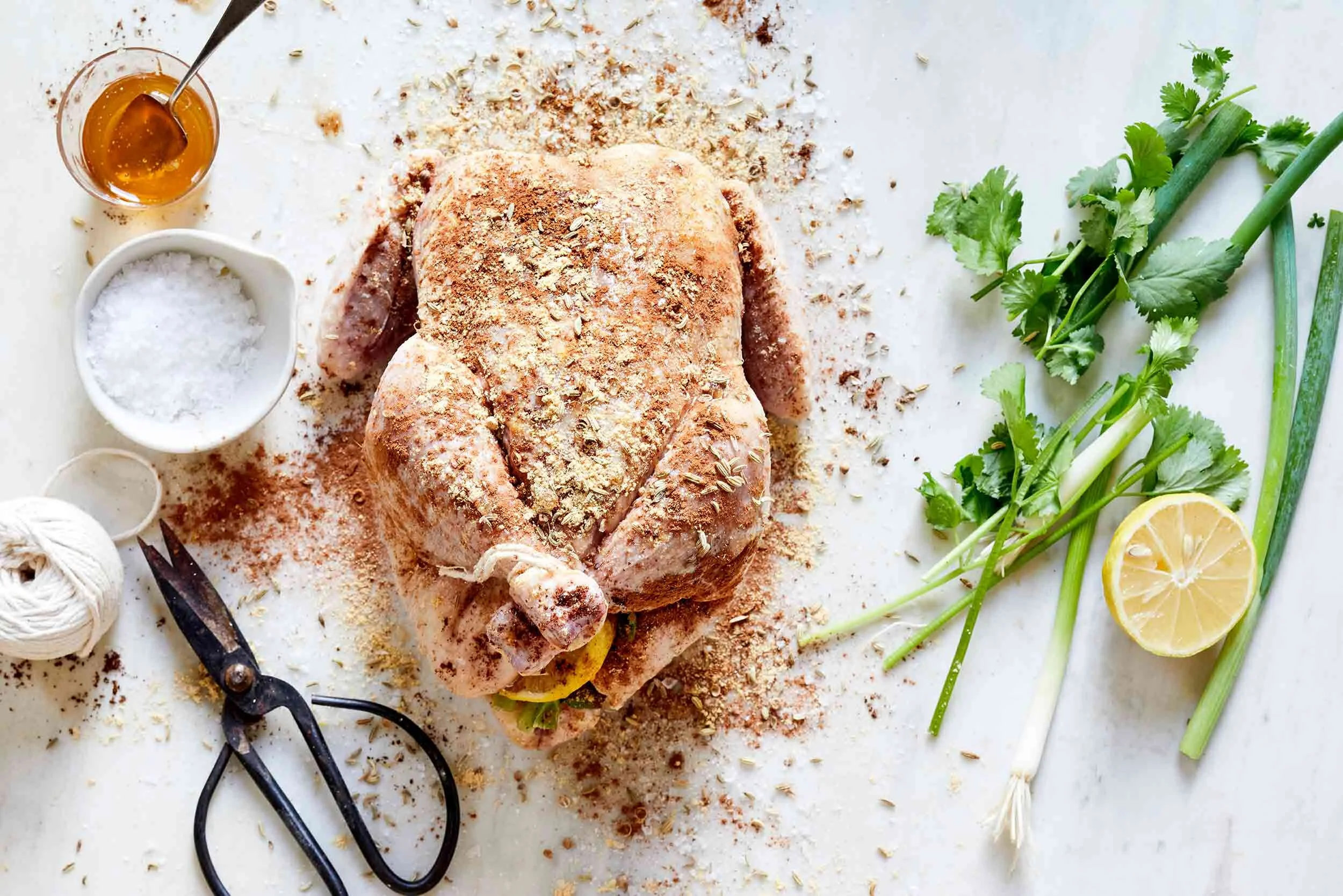A whole chicken on a sheet pan being patted dry and sprinkled with salt and pepper on a home kitchen counter