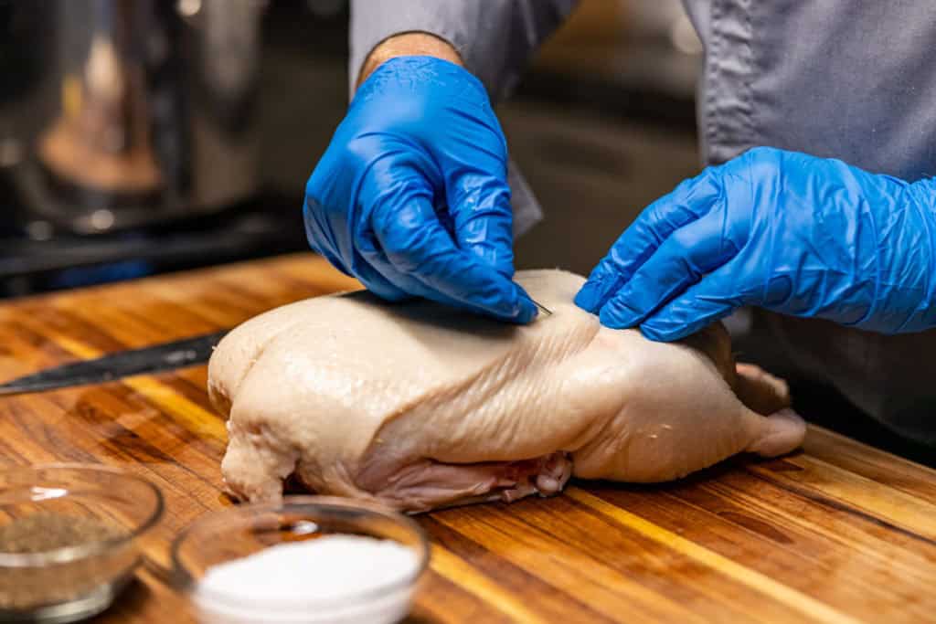 A whole duck on a cutting board with the skin being gently pricked using a skewer to help fat render