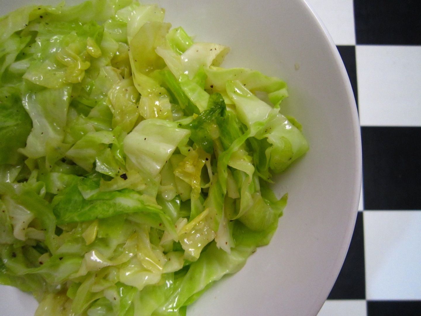 A whole green cabbage on a cutting board with kosher salt, black pepper, butter, garlic cloves, and a lemon on a kitchen counter