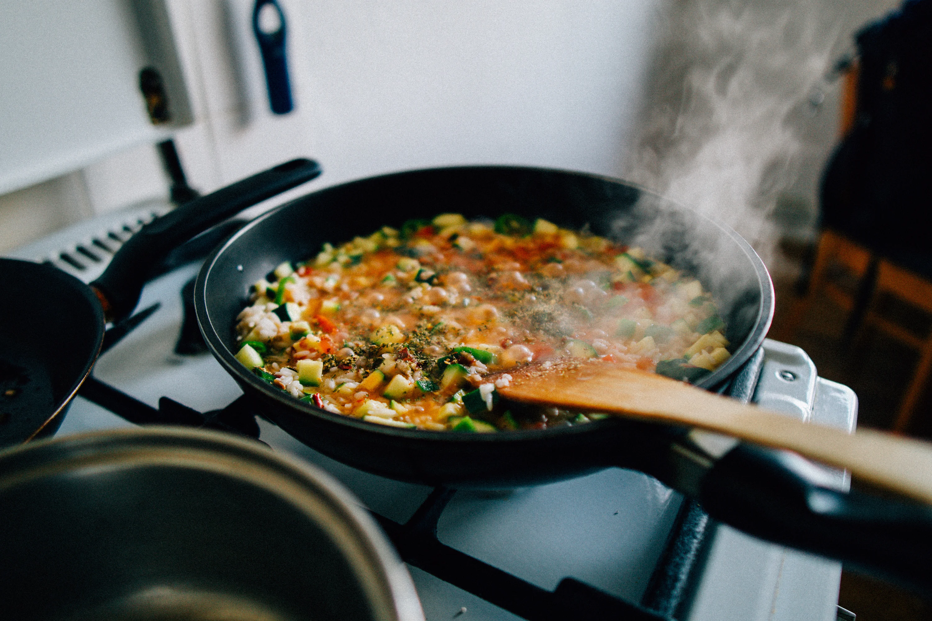 A wide skillet and a lidded pot sitting on a home stove with a wooden spoon resting on a clean utensil spoon rest