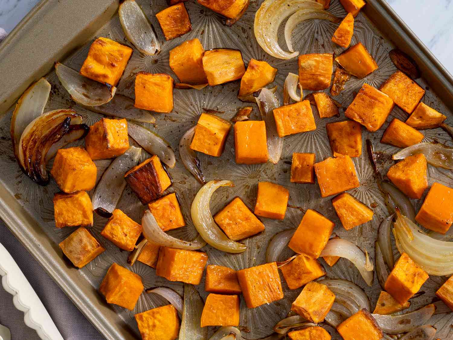 A wooden cutting board covered with evenly diced sweet potato cubes next to a chef’s knife on a bright kitchen counter