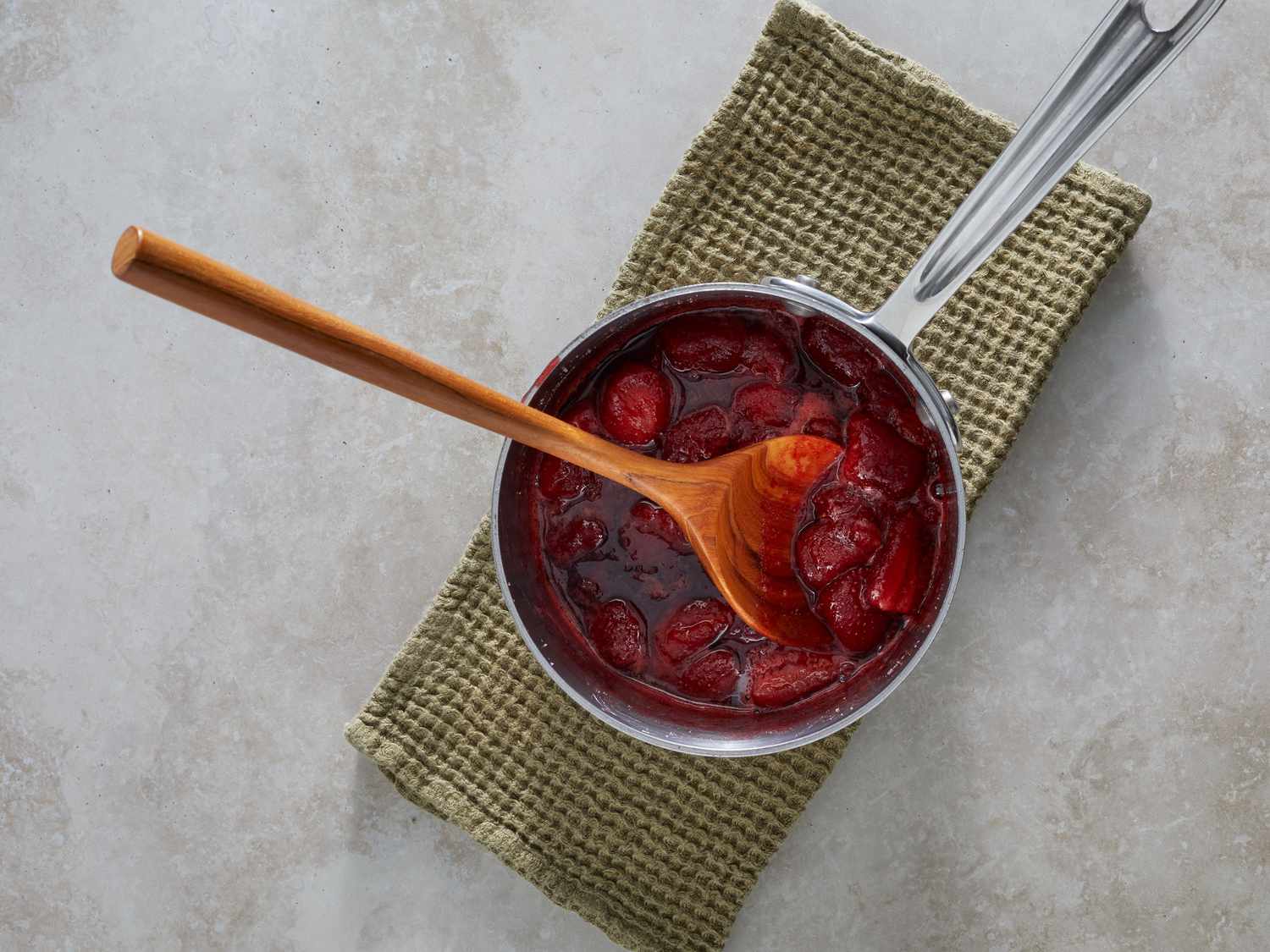 A wooden spoon dragging through thick strawberry reduction in a saucepan, leaving a clean trail