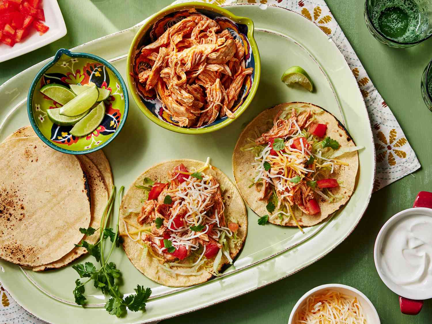 A wooden spoon scooping shredded salsa chicken from a pot, with steam rising and bits of tomato and green chile visible