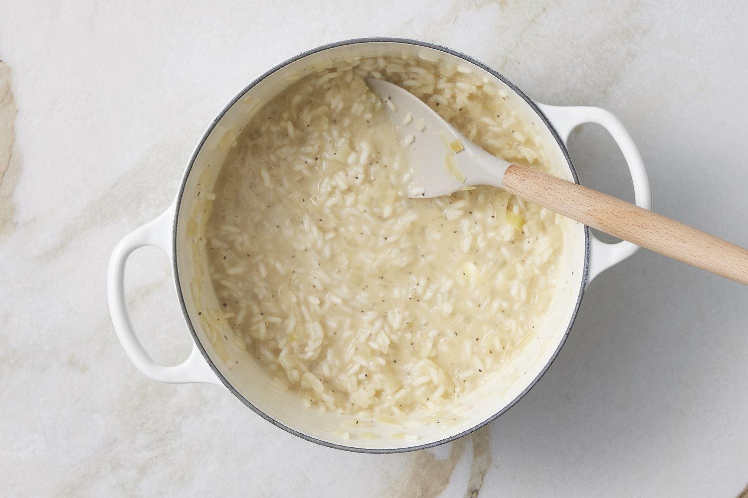 A wooden spoon stirring creamy risotto in a wide pot on a stovetop with steam rising under warm kitchen lighting