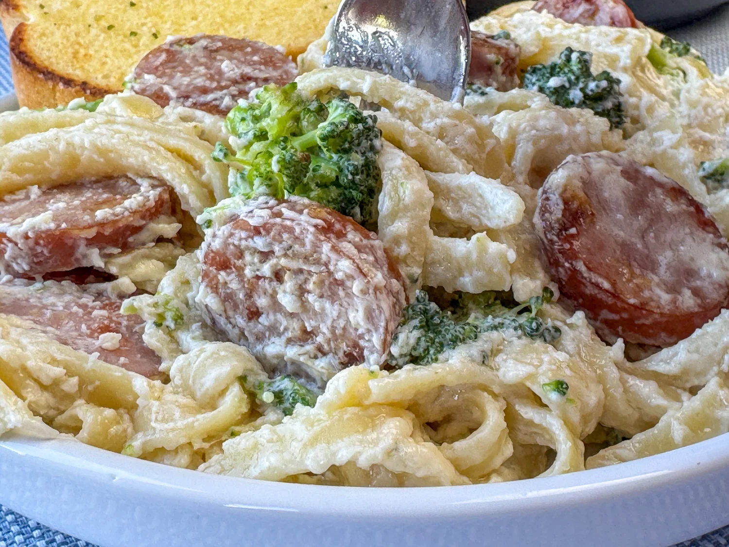 A wooden spoon stirring creamy tomato pasta with kielbasa in a deep skillet on a stovetop