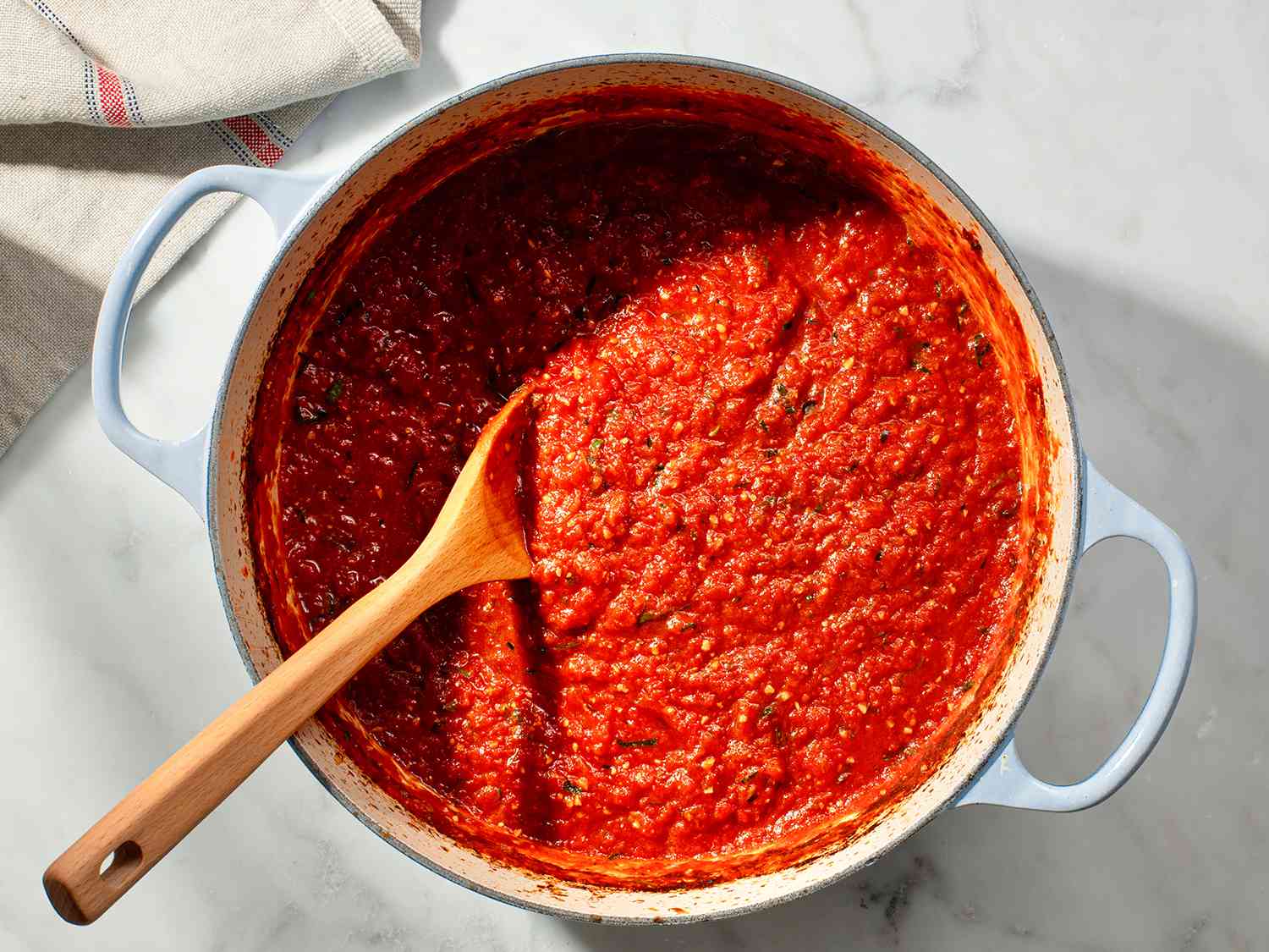 A wooden spoon stirring thickened classic red pasta sauce in a pot