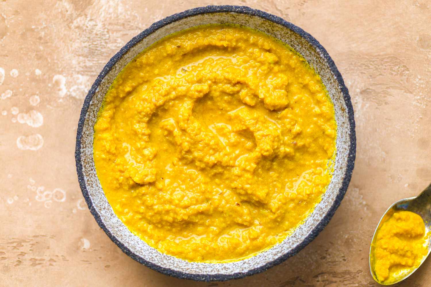 A wooden spoon stirring yellow curry paste with onions in a pot, the mixture turning glossy as it fries
