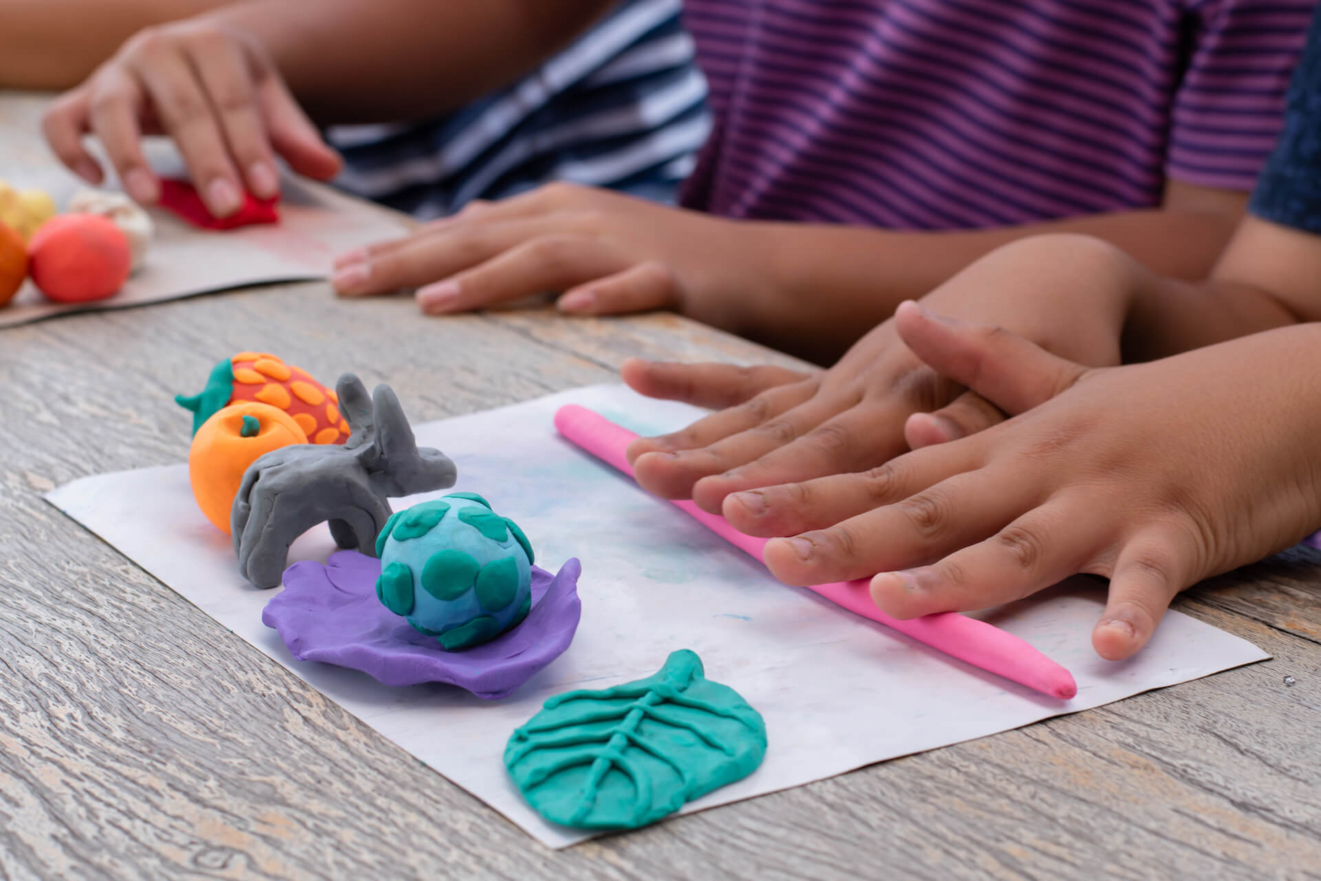 Adult hands kneading a ball of play dough on a lightly floured kitchen counter.