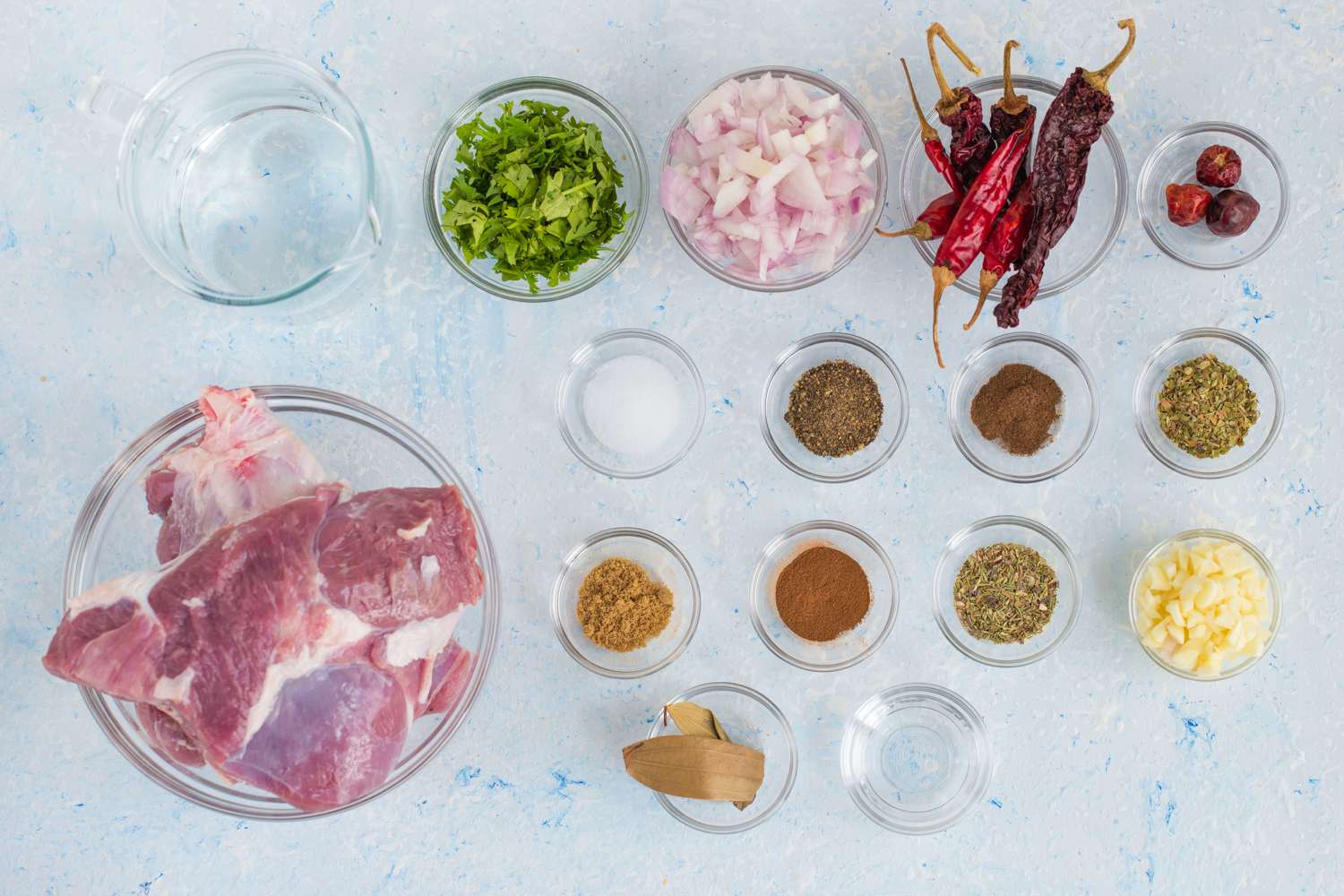 All birria ingredients arranged on a kitchen counter including dried chiles, beef chunks, onions, garlic, spices, tortillas, and cheese
