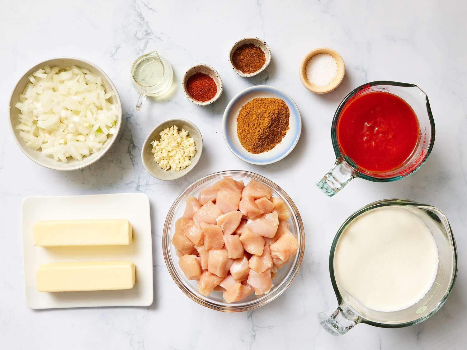 All butter chicken ingredients arranged on a clean kitchen counter, including chicken thighs, yogurt, spices, canned tomatoes, cream, butter, garlic, ginger, and cilantro