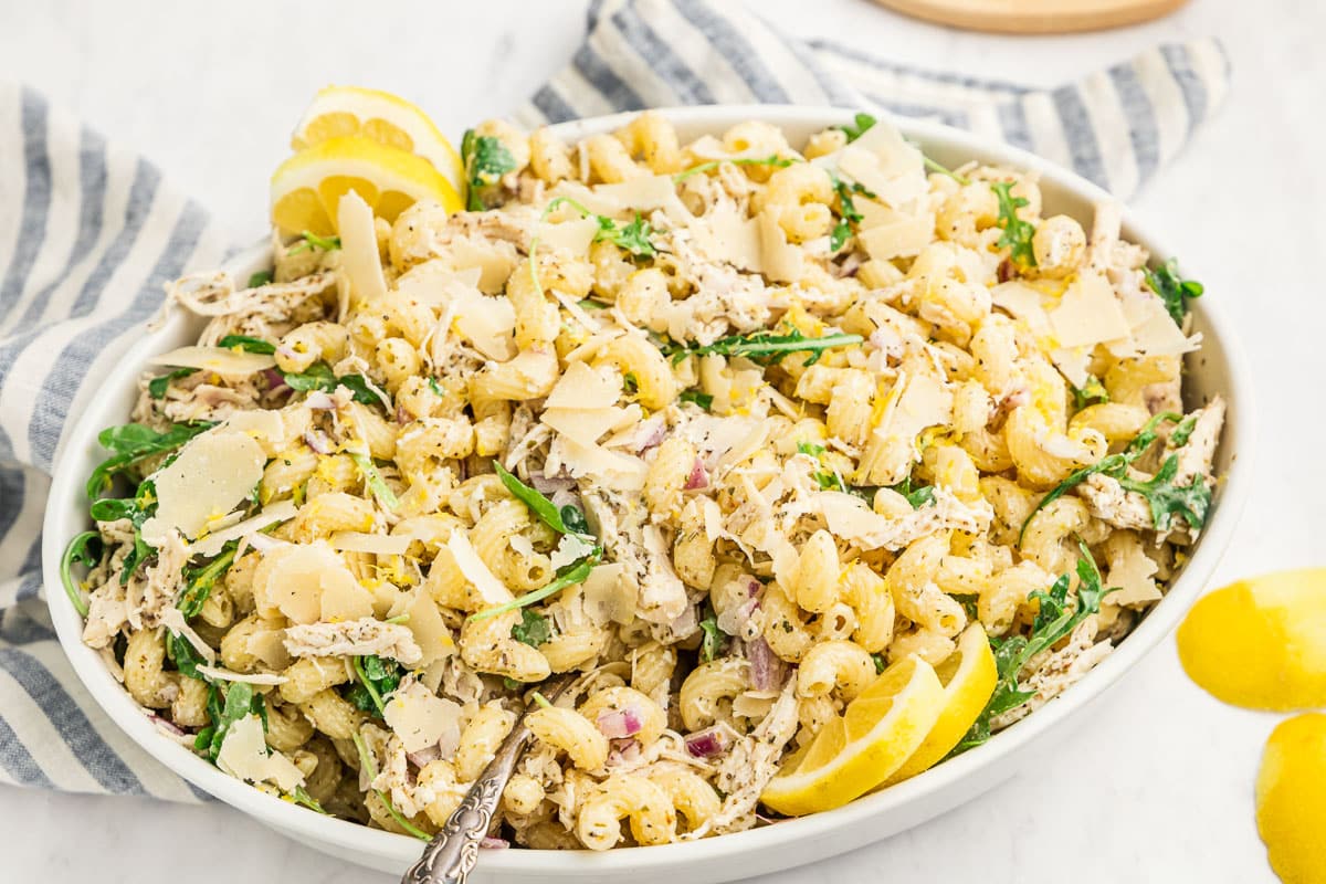 All ingredients for a creamy Italian pasta salad dressing arranged on a kitchen counter, including mayonnaise, olive oil, red wine vinegar, Dijon mustard, garlic, dried oregano, dried basil, finely grated Parmesan, salt, pepper, and a lemon