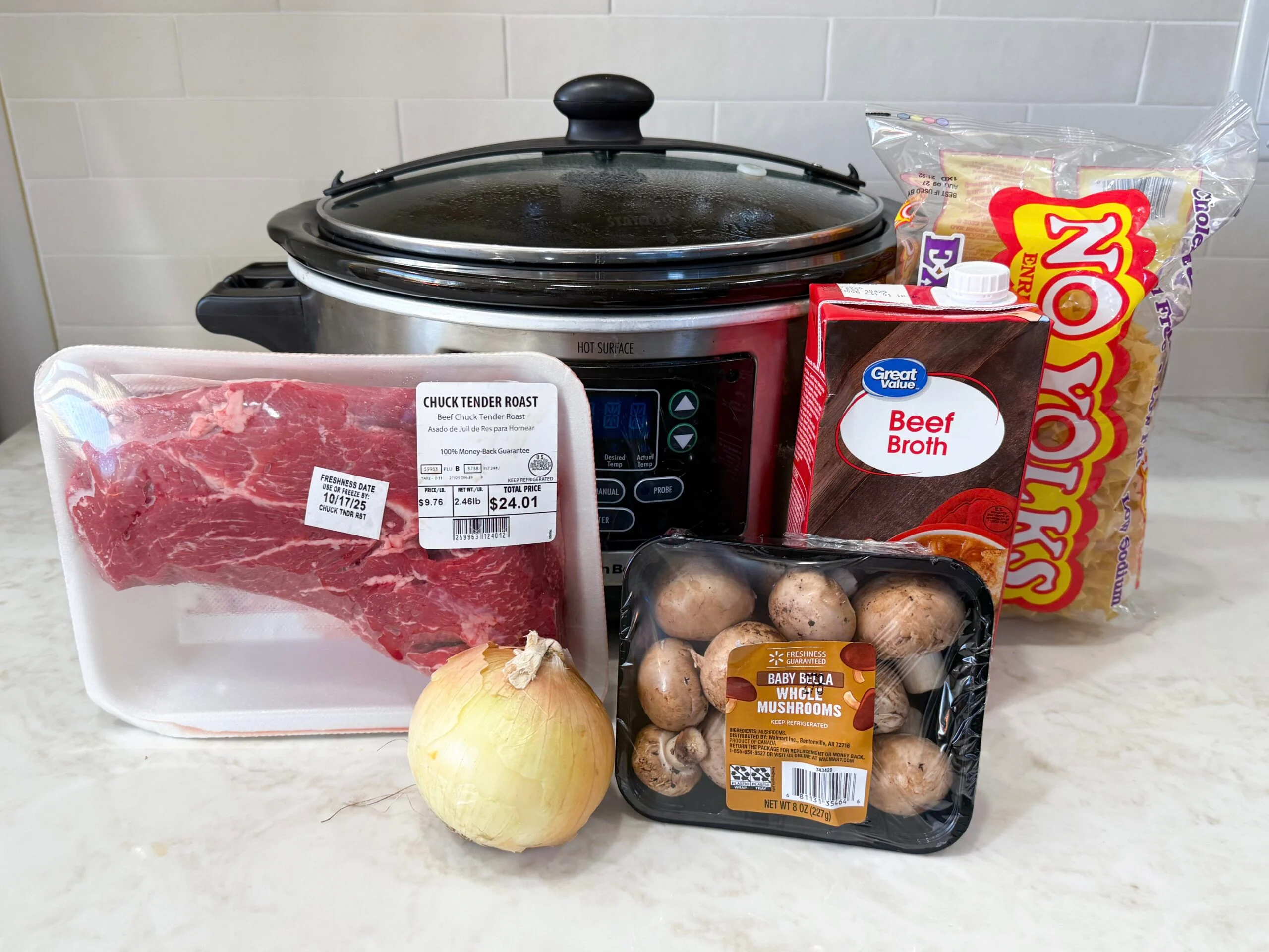 All ingredients for crock pot beef stroganoff arranged on a kitchen counter, including beef chuck, mushrooms, onions, garlic, broth, Worcestershire, sour cream, and egg noodles
