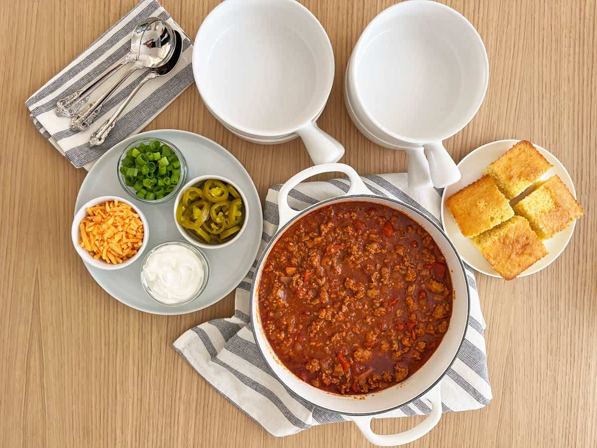 All ingredients for no bean chili laid out on a clean kitchen counter including ground beef, onions, garlic, tomato paste, crushed tomatoes, broth, and small bowls of spices in warm natural light