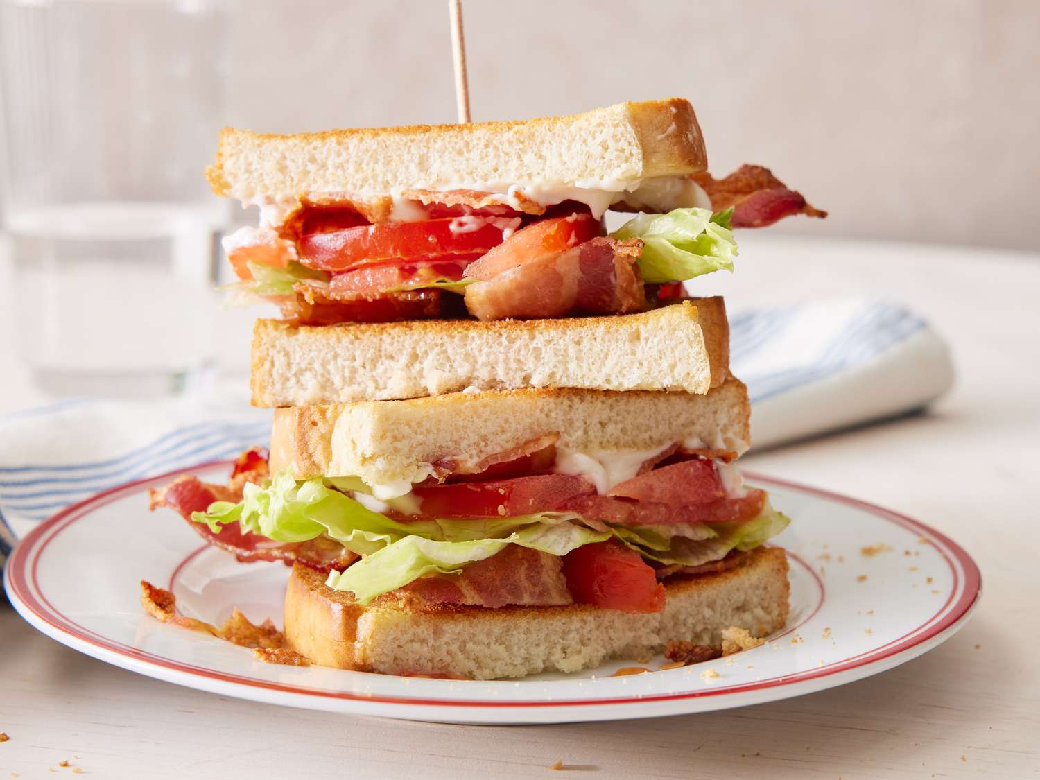 All the BLT ingredients arranged on a kitchen counter, including bacon, ripe tomatoes, lettuce, sliced bread, mayonnaise, lemon, salt, and black pepper