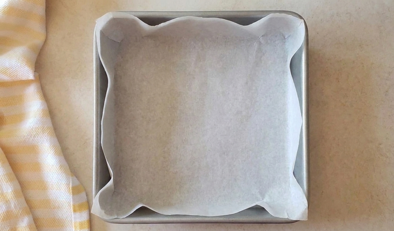 An 8x8 baking pan lined with parchment paper, ready for brownie batter