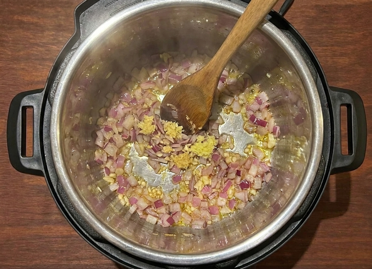 An Instant Pot inner pot with onions, garlic, and ginger sautéing, a wooden spoon stirring as steam rises