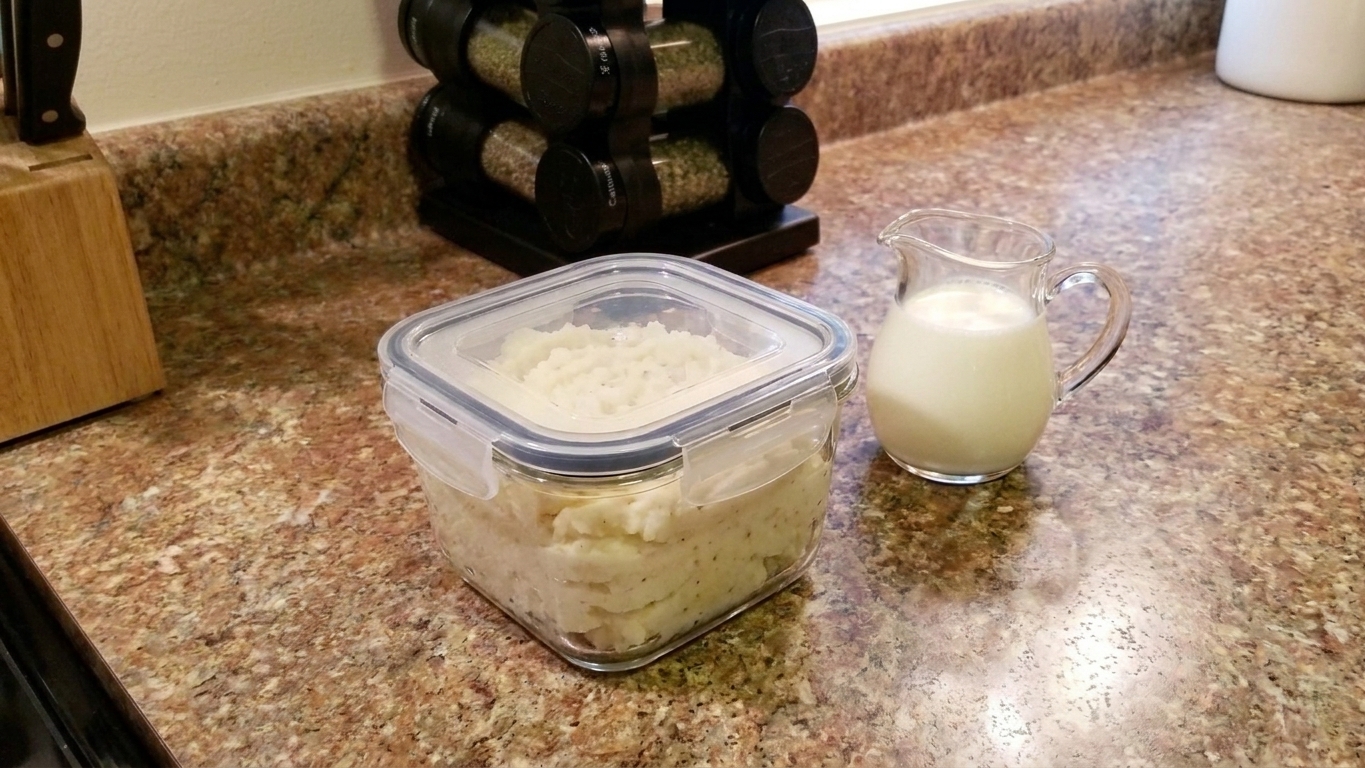 An airtight container filled with leftover whipped potatoes on a kitchen counter with a small pitcher of cream nearby