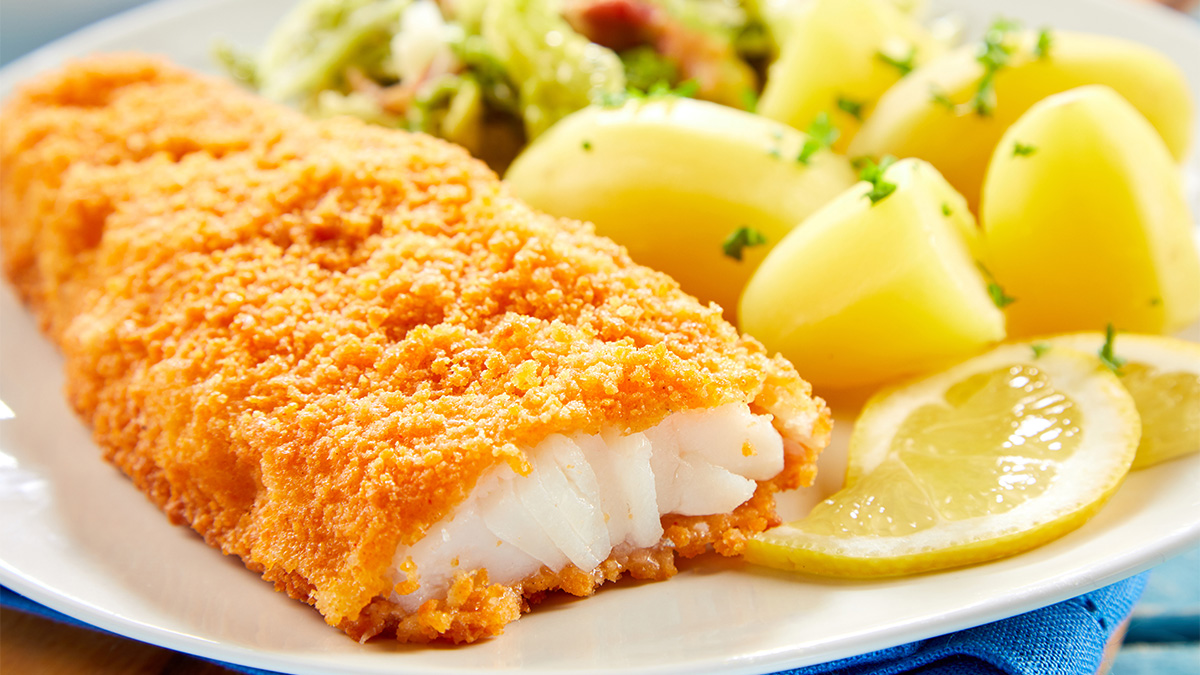 An airtight container holding leftover beer battered fish on a kitchen counter, with paper towels lining the bottom to absorb moisture