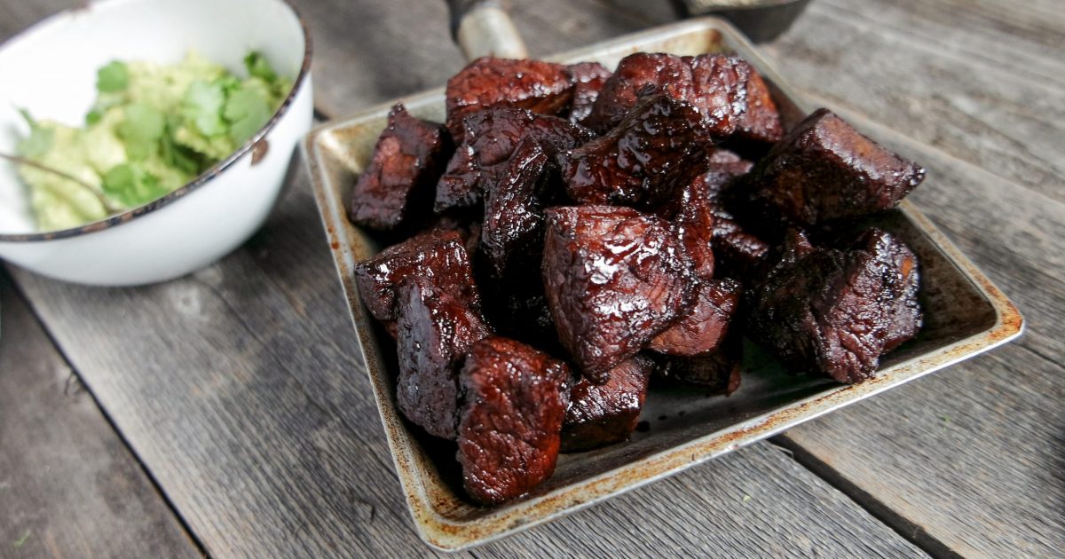 An airtight glass container filled with cooked steak tips and a little pan sauce, sitting on a bright kitchen counter near a refrigerator