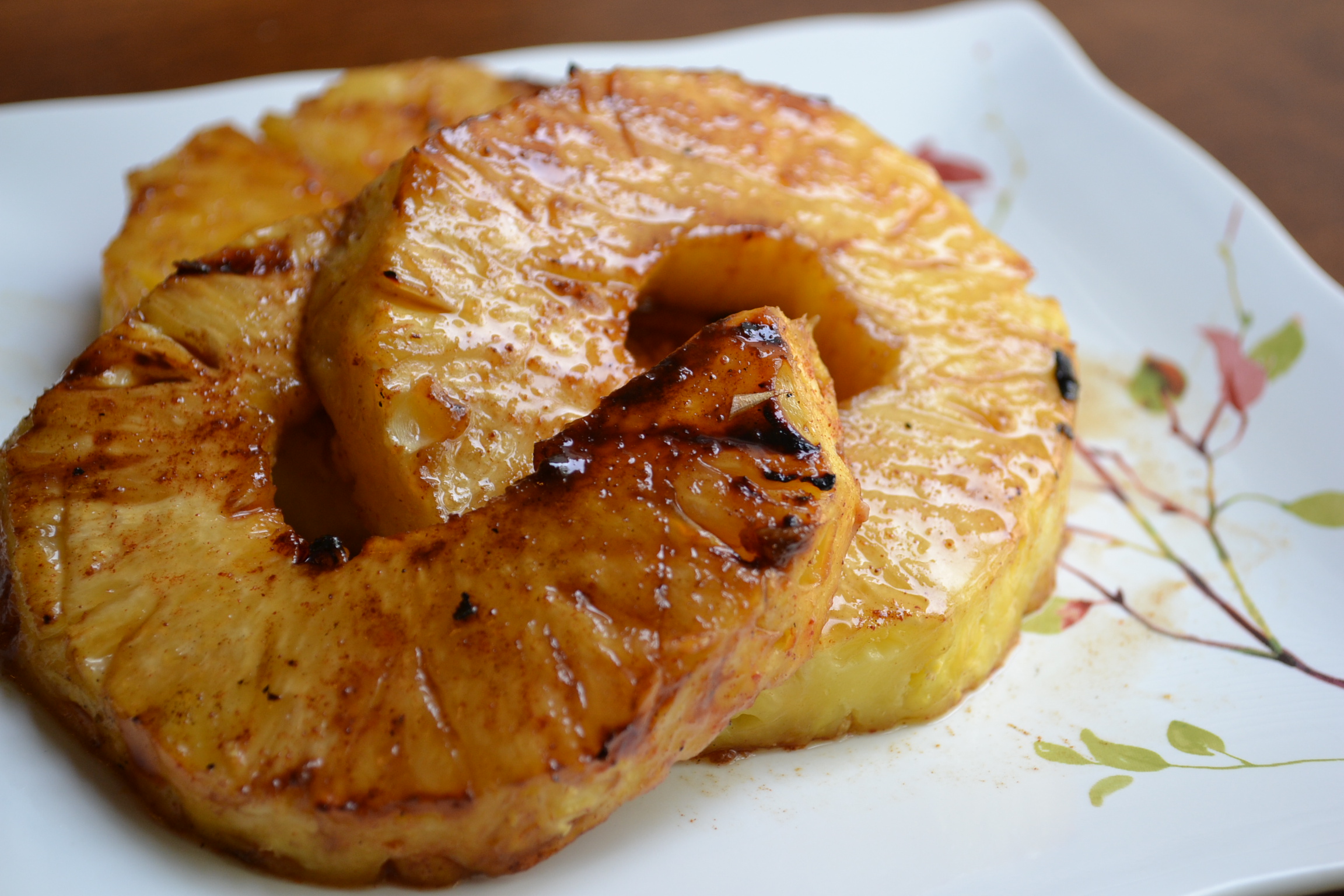 An airtight glass container filled with grilled pineapple spears in a refrigerator setting, with a small cup of glaze beside it