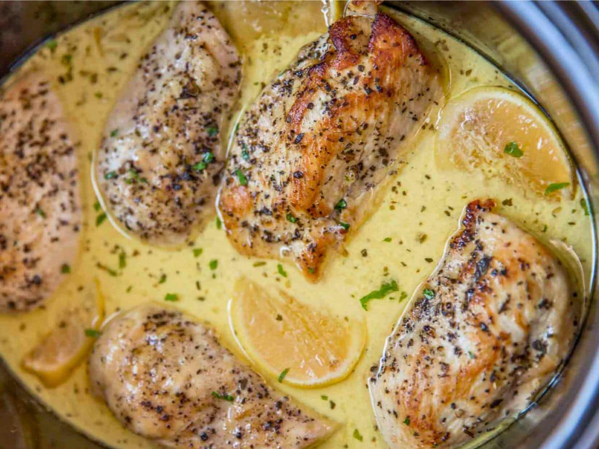 An airtight glass container filled with leftover lemon chicken and sauce sitting on a kitchen counter next to its lid