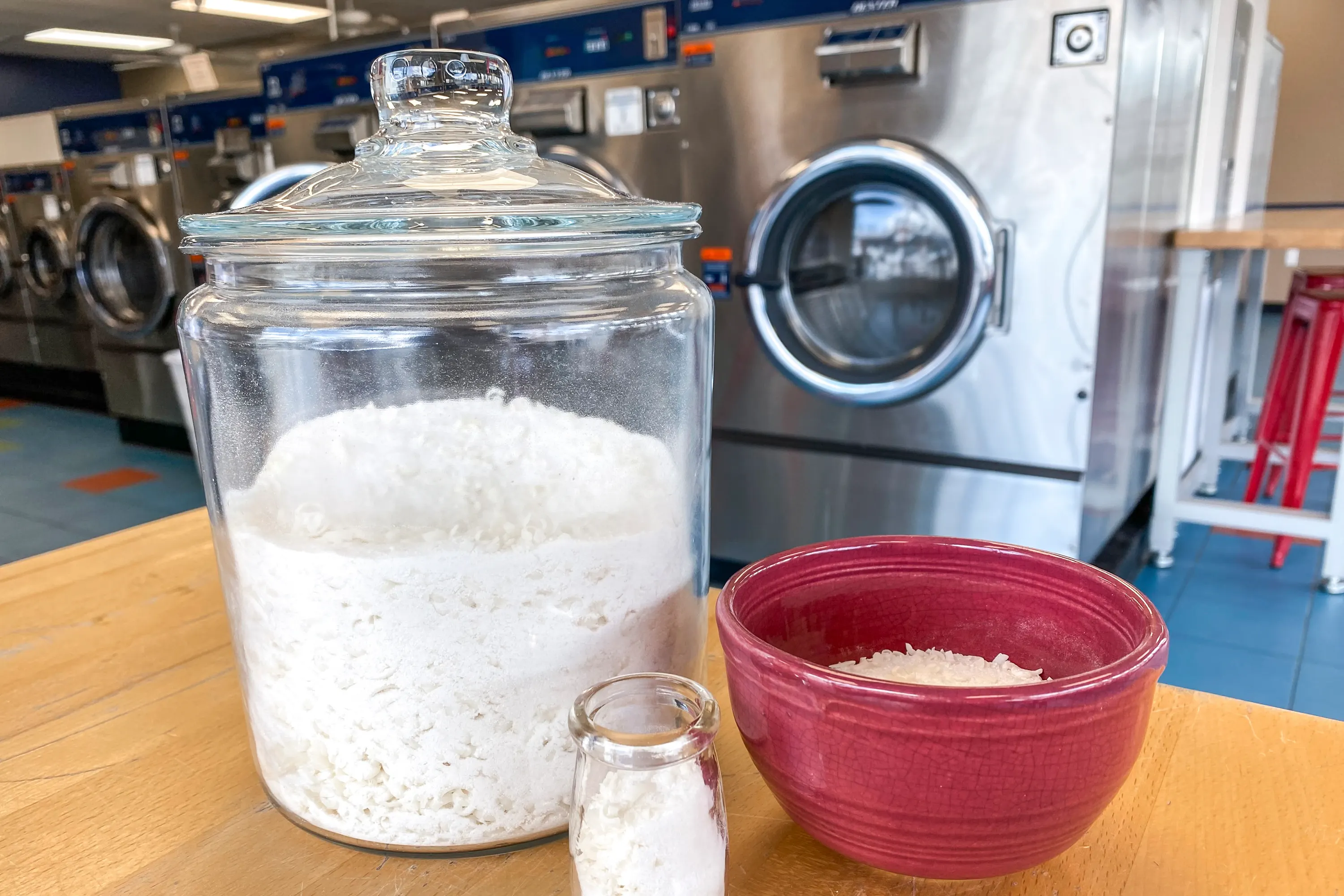 An airtight glass jar filled with homemade powdered laundry wash on a laundry room shelf next to a tablespoon measuring spoon