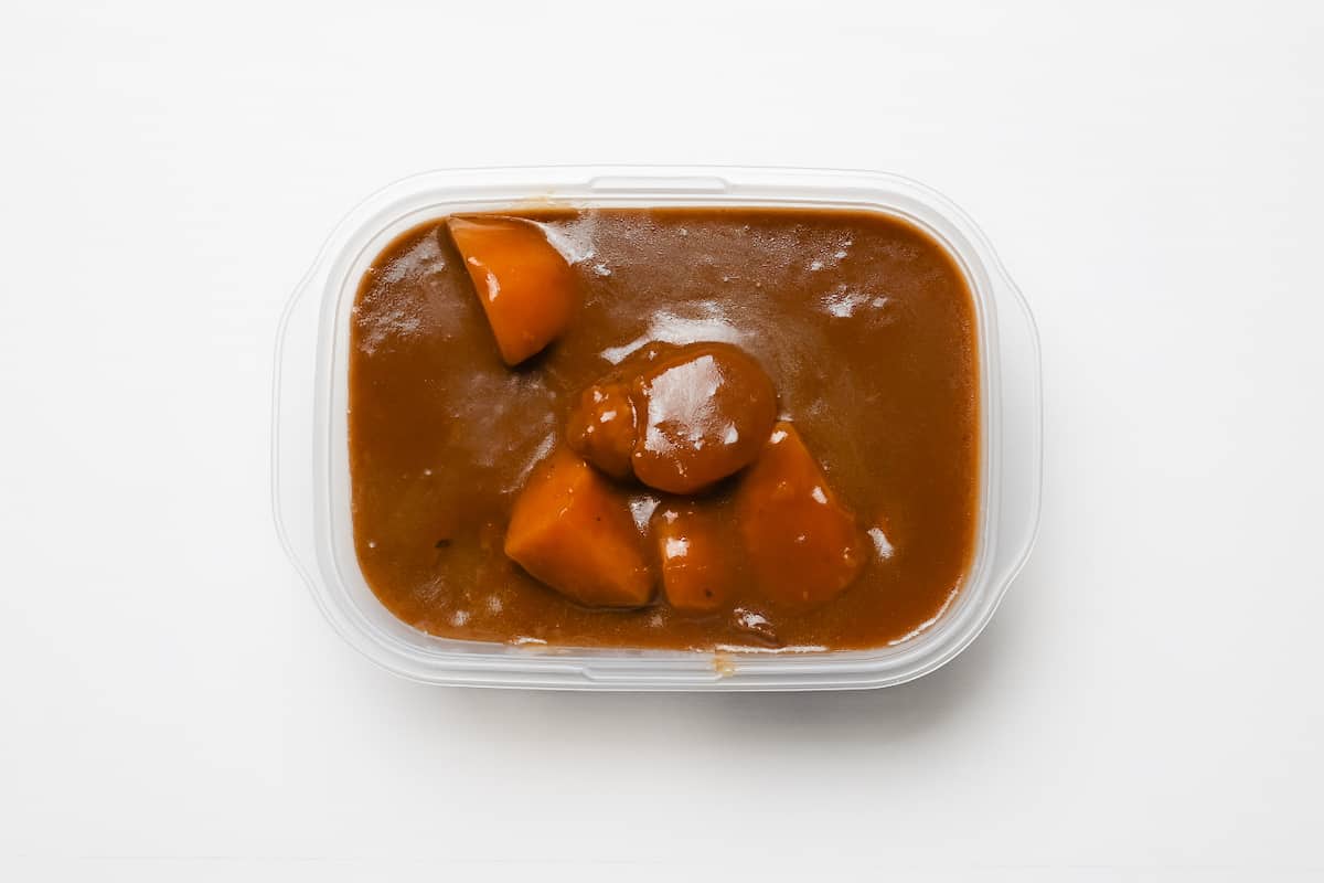 An airtight glass meal prep container filled with leftover Japanese curry, cooled and ready for the refrigerator on a kitchen counter