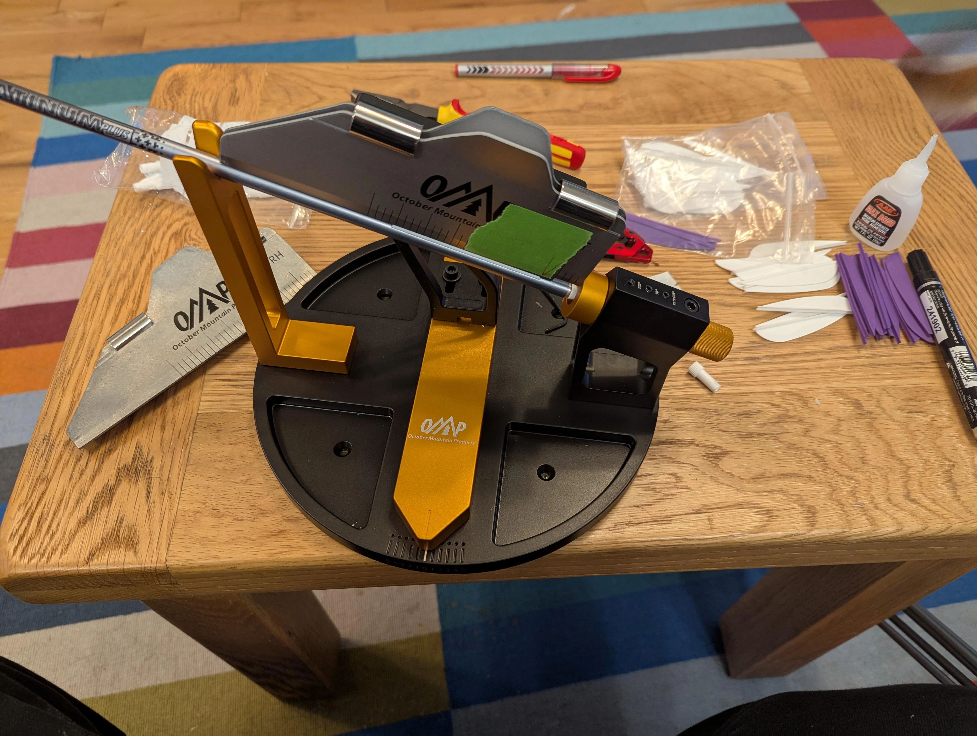 An arrow fletching jig clamped to a clean table with a few carbon arrows lined up beside a small parts tray