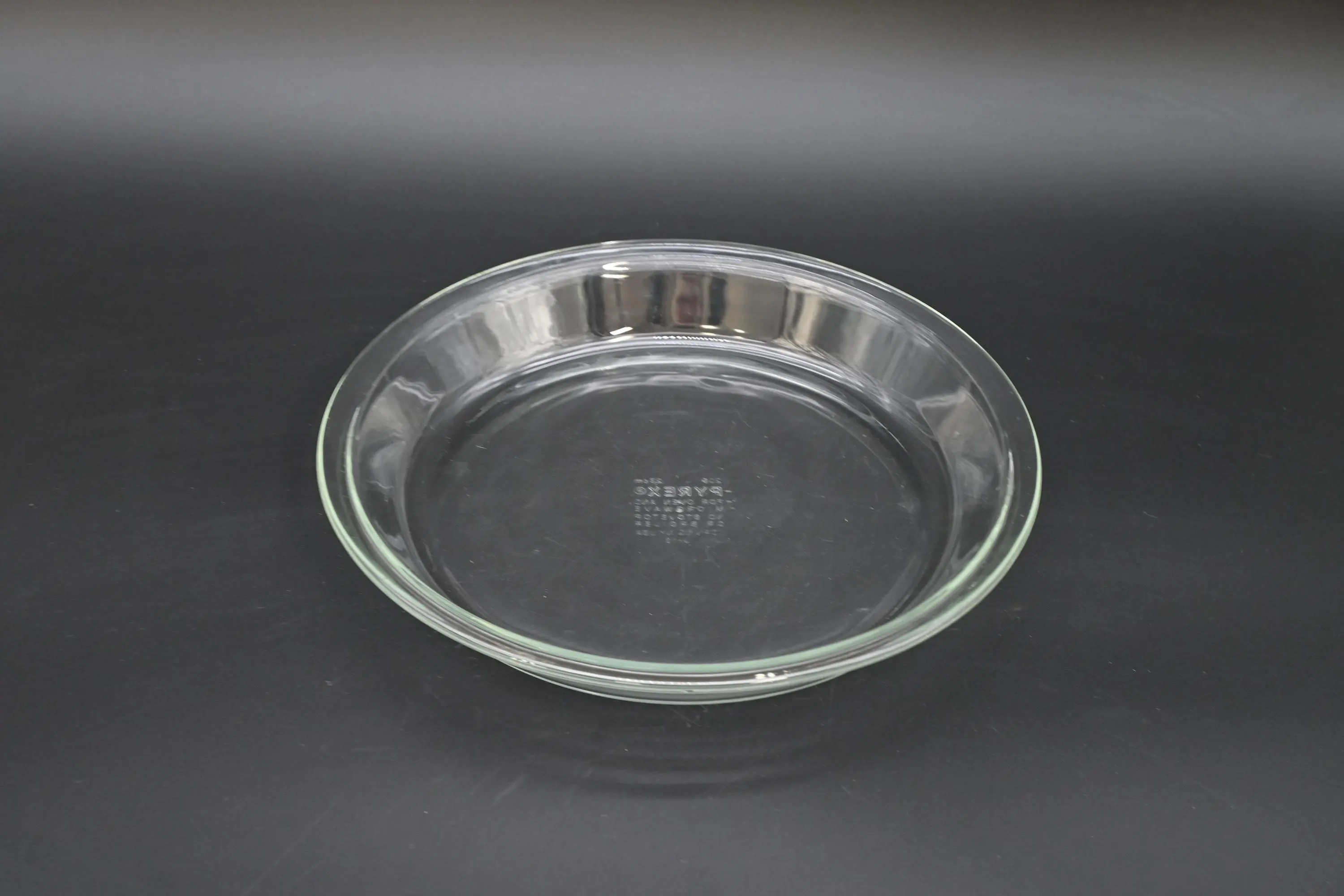 An empty 9-inch glass pie plate on a clean kitchen counter with a whisk and mixing bowl nearby