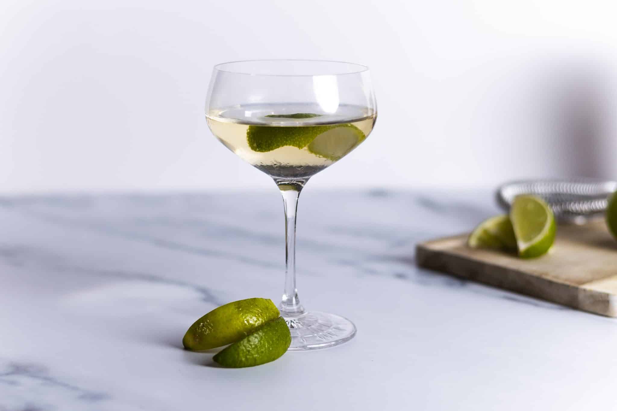 An ice-cold vodka gimlet in a chilled coupe glass with a thin lime wheel on the rim, set on a kitchen counter